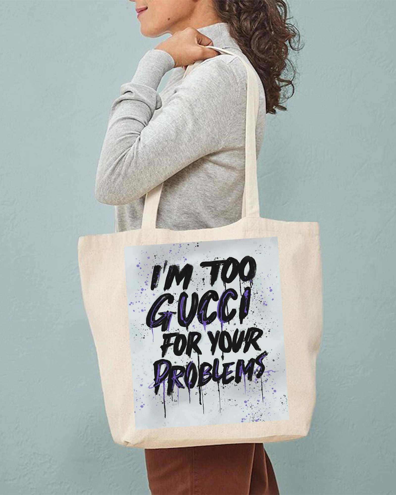 Person holding a tote bag with 'I'm too Gucci for your problems' text against a plain background