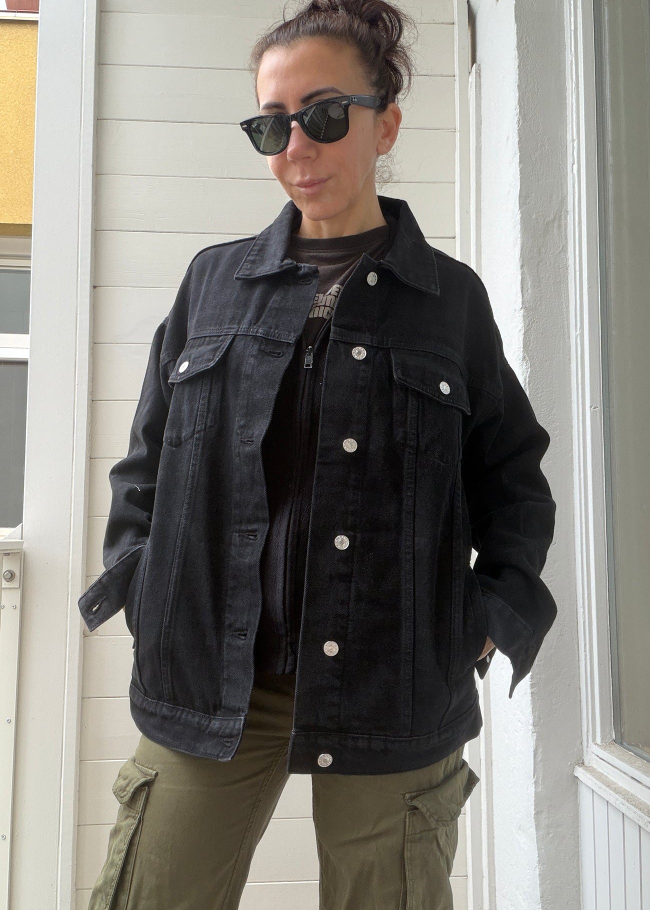 Person wearing a black denim jacket and green cargo pants standing indoors.