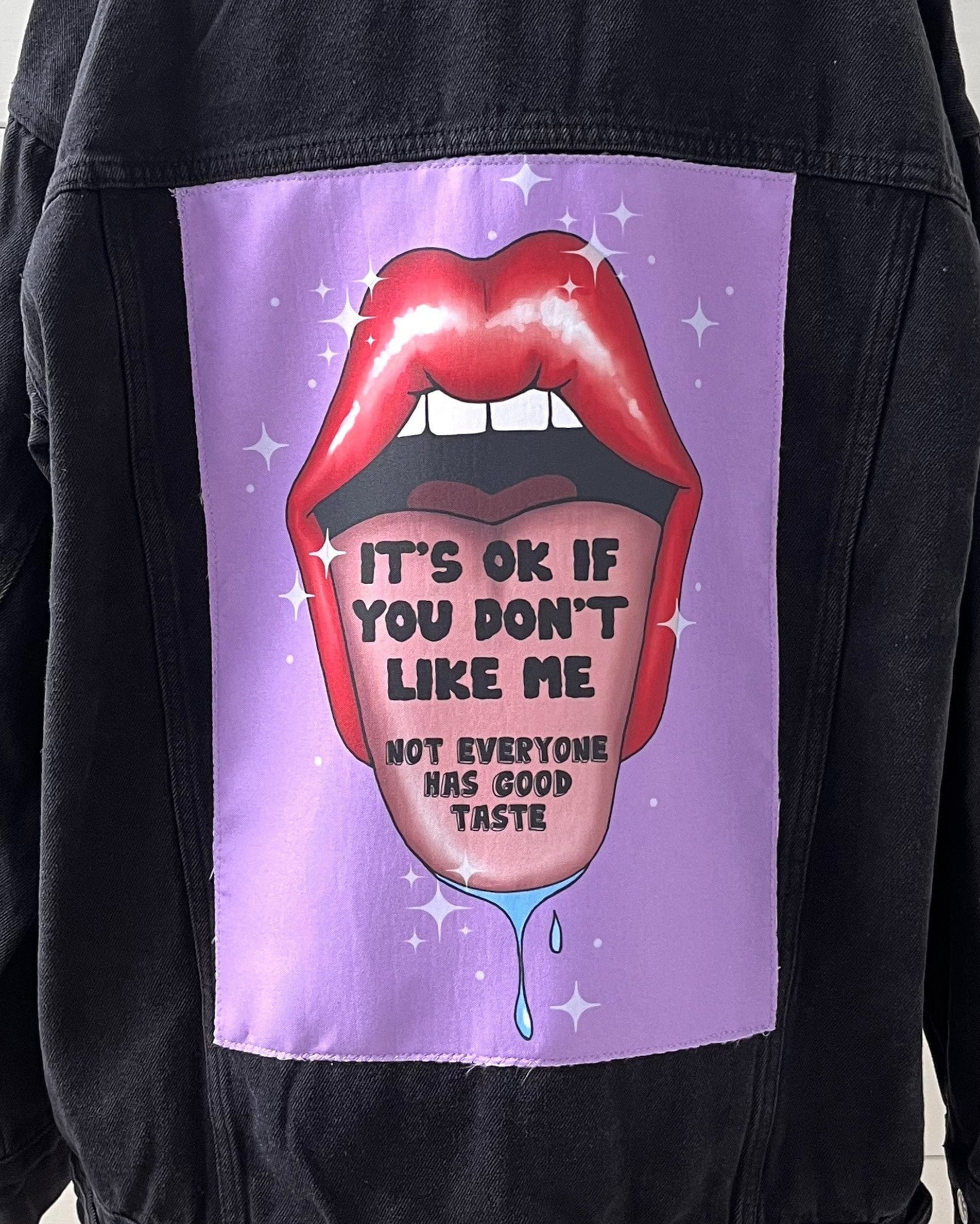 A denim jacket with a patch on the back featuring an illustration of a mouth with text, sewn on as a decoration.