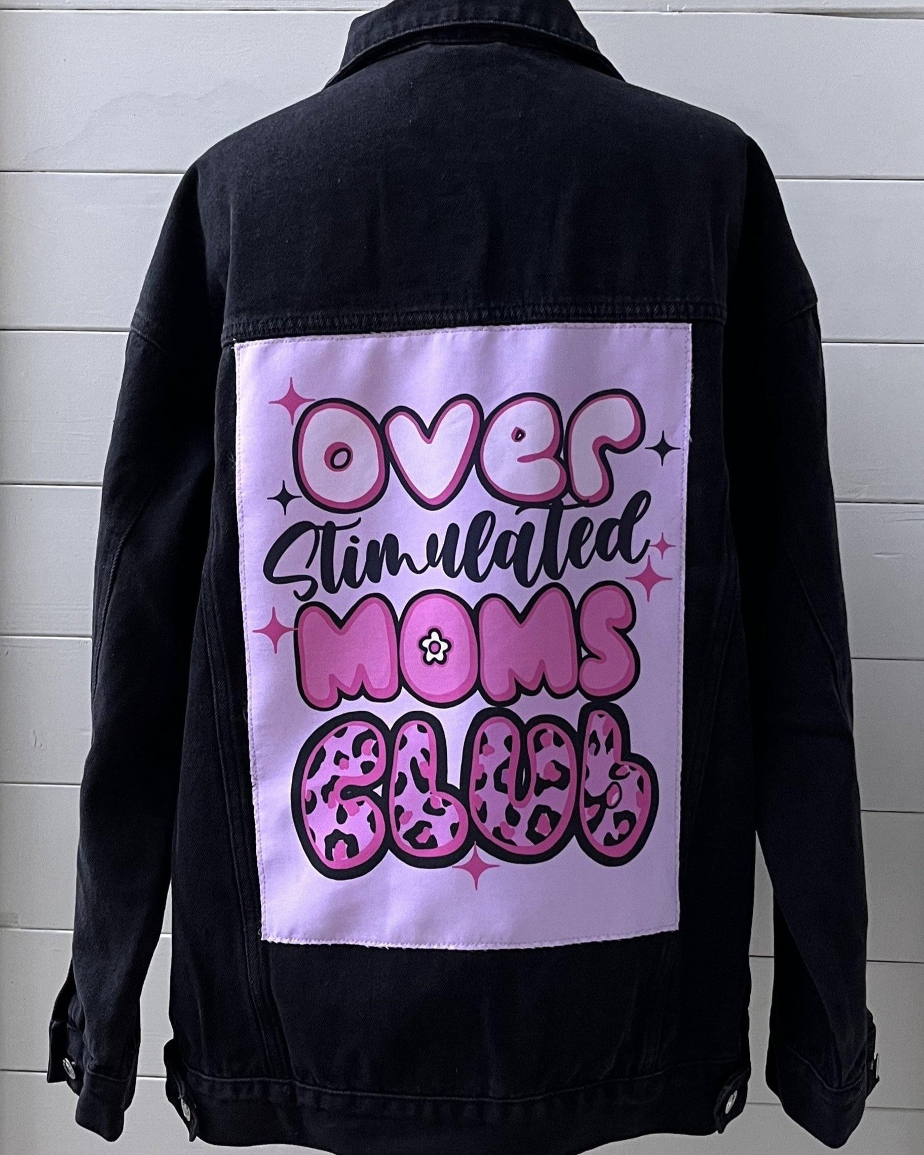 Black denim jacket with a pink graphic on the back against a white wooden panel background