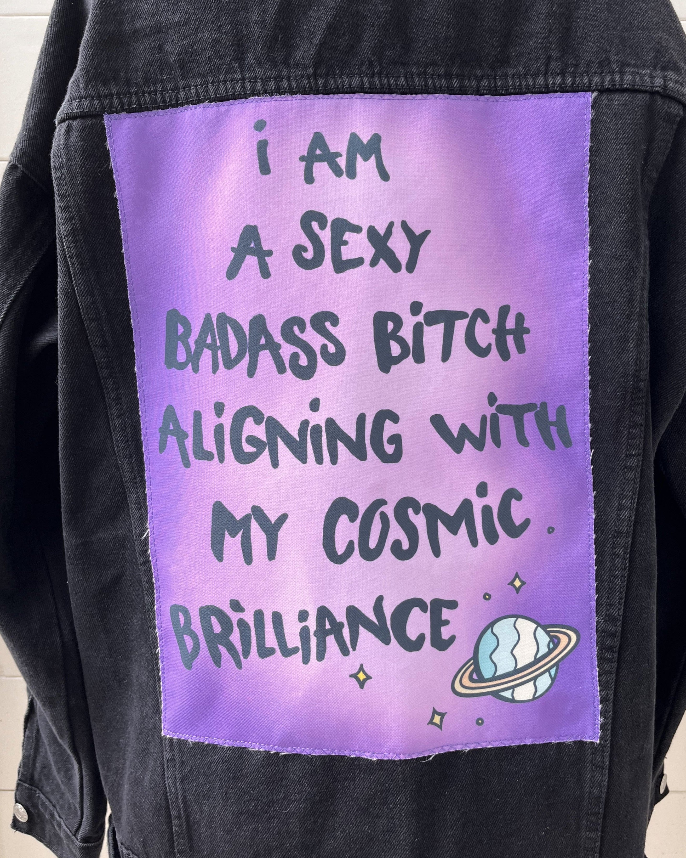 A denim jacket with a purple back patch featuring text and a graphic design.