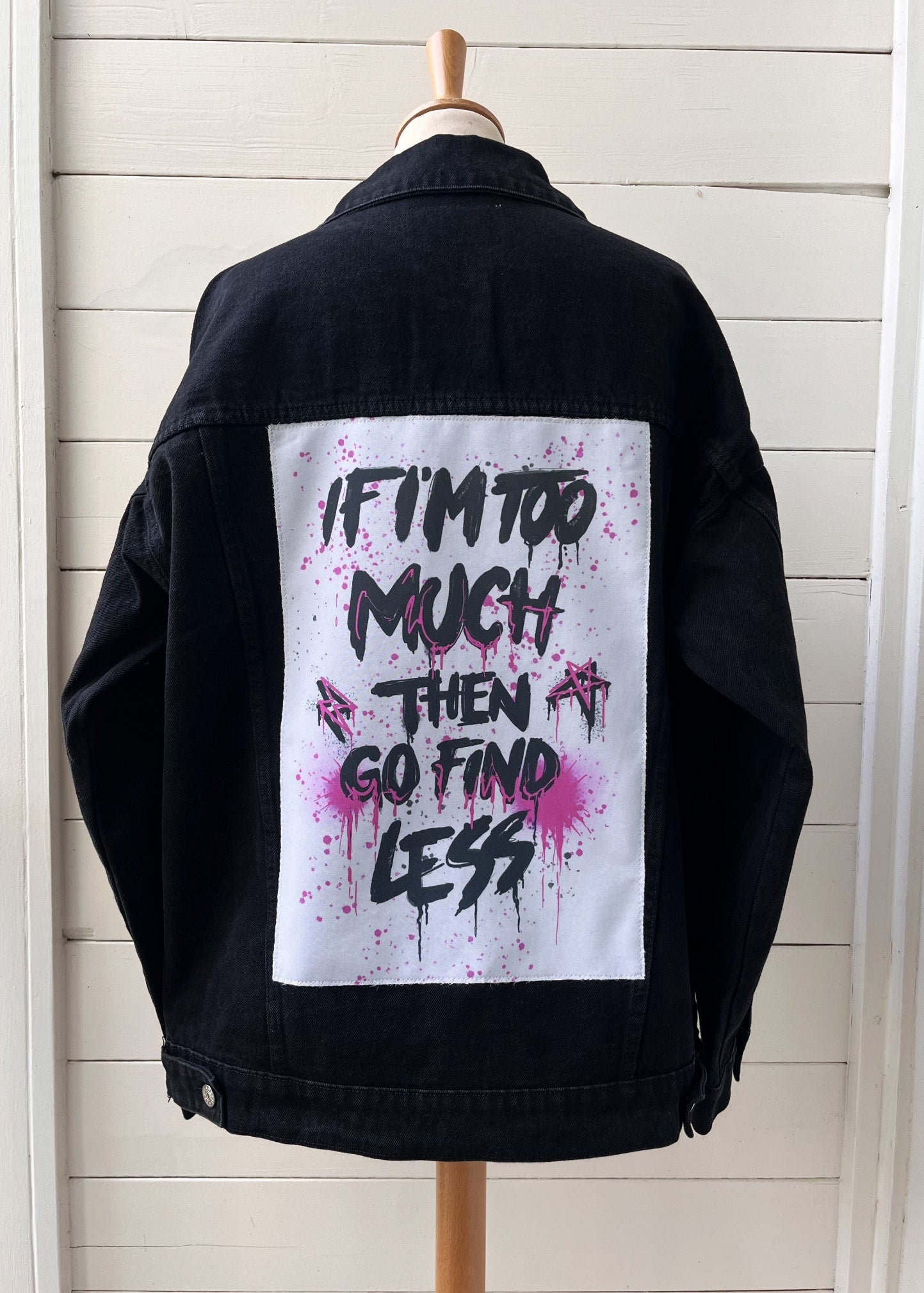 A denim jacket with a 'If I'm too much... then go find less' text patch on the back.