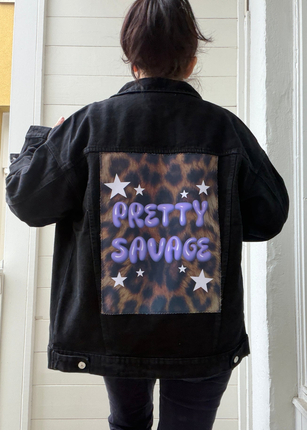 Person wearing a black jacket with 'Pretty Savage' text and leopard print design.