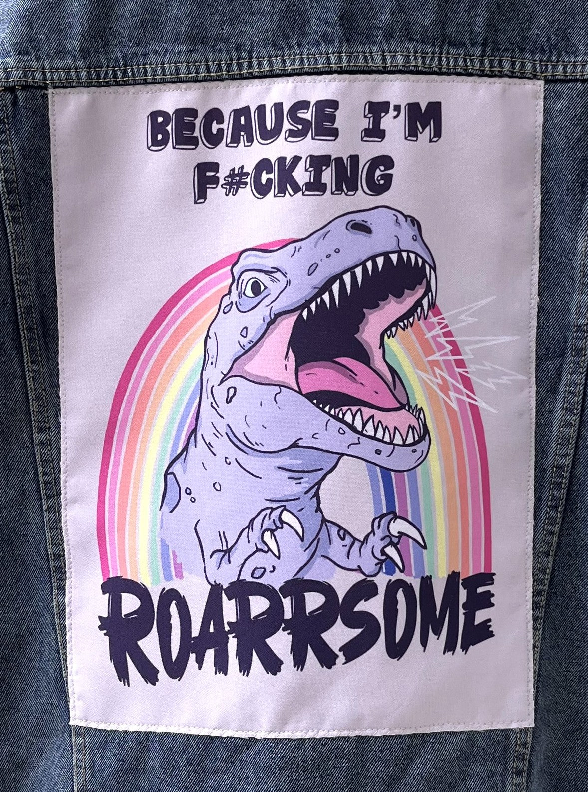 Patch with a dinosaur and rainbow design on a denim jacket