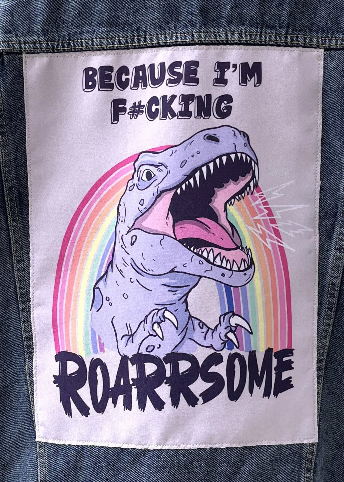 Patch with a dinosaur and rainbow design on a denim jacket