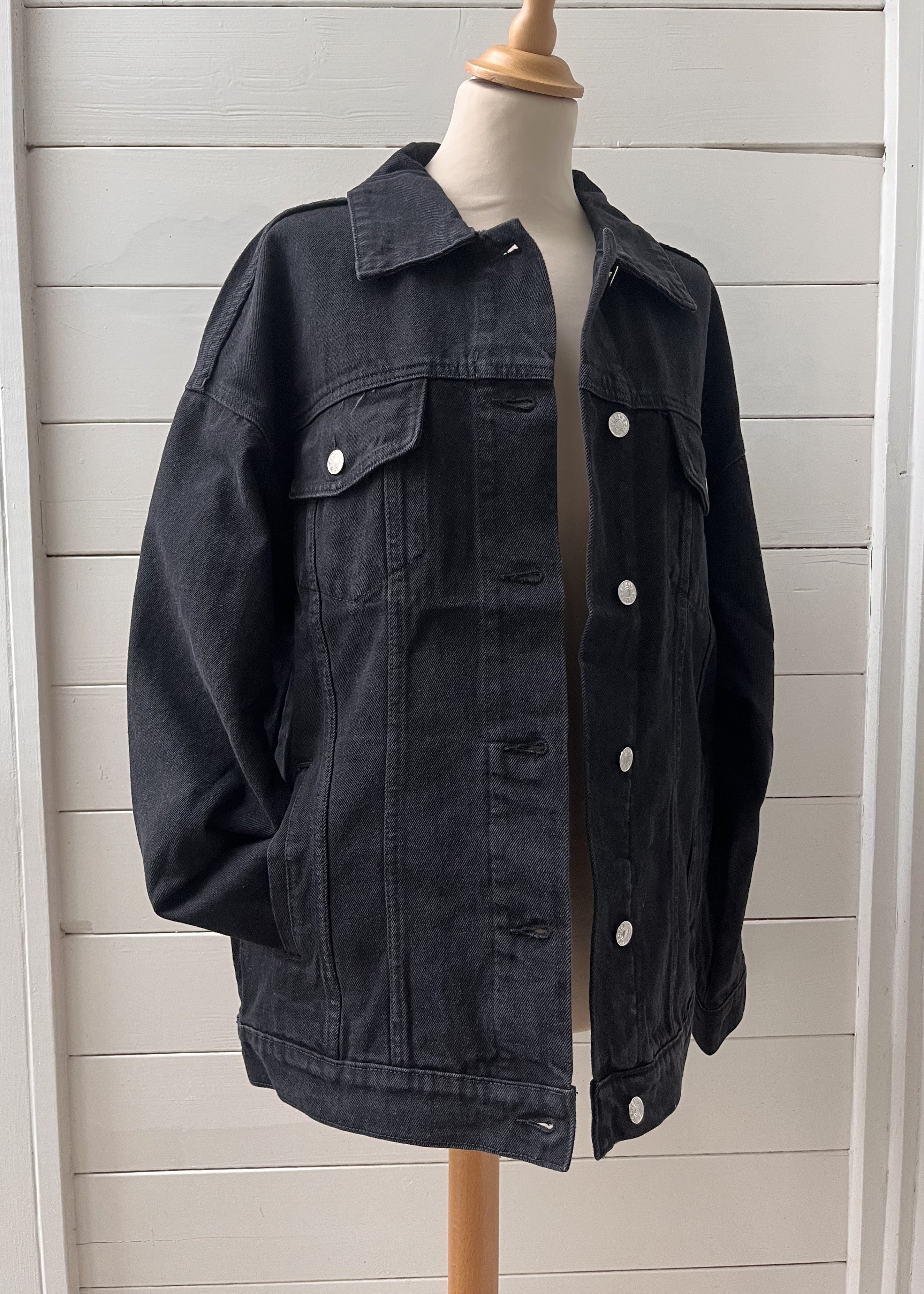 Black denim jacket on a mannequin against a white wooden panel background