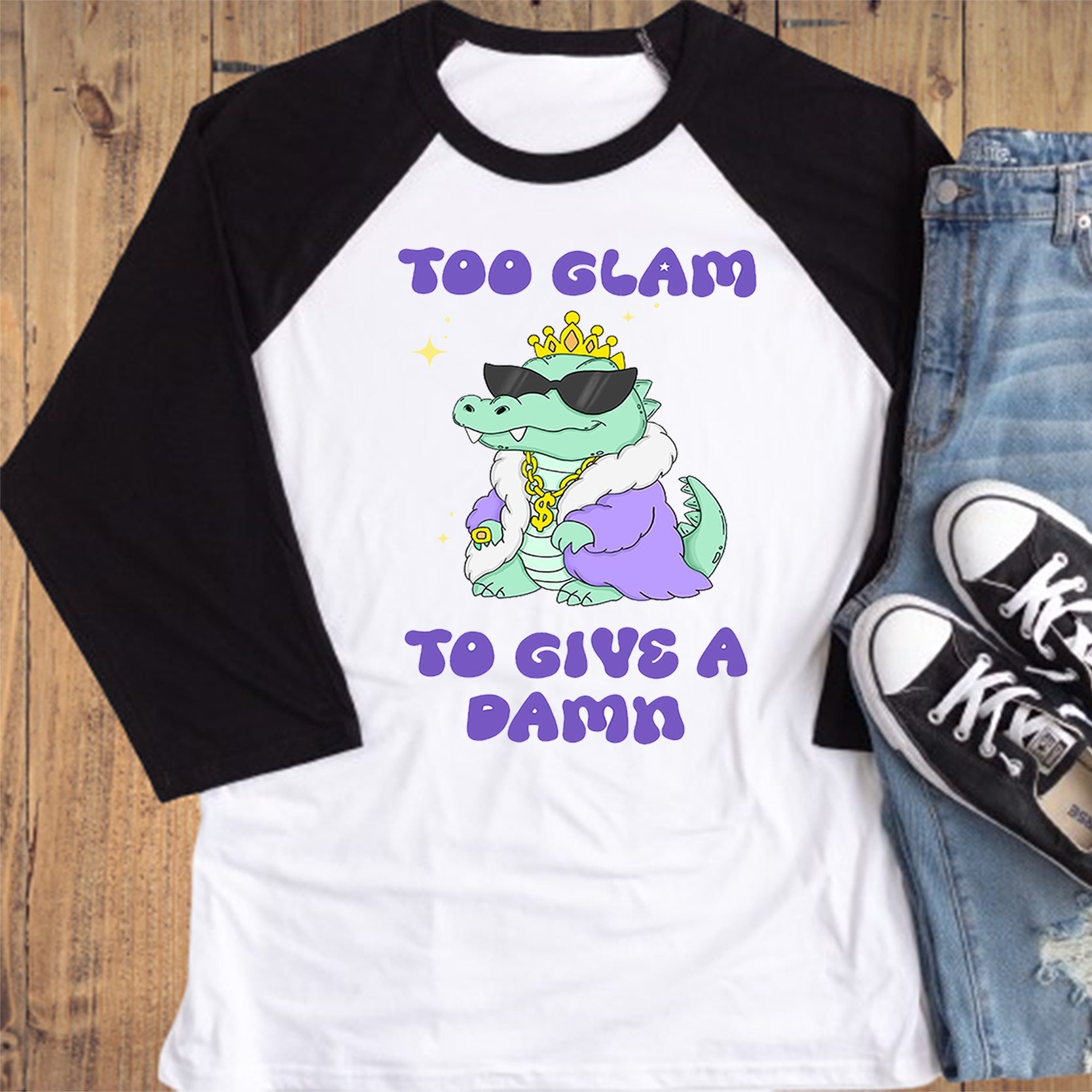 White baseball shirt with graphic design and text, paired with jeans and sneakers on a wooden surface.