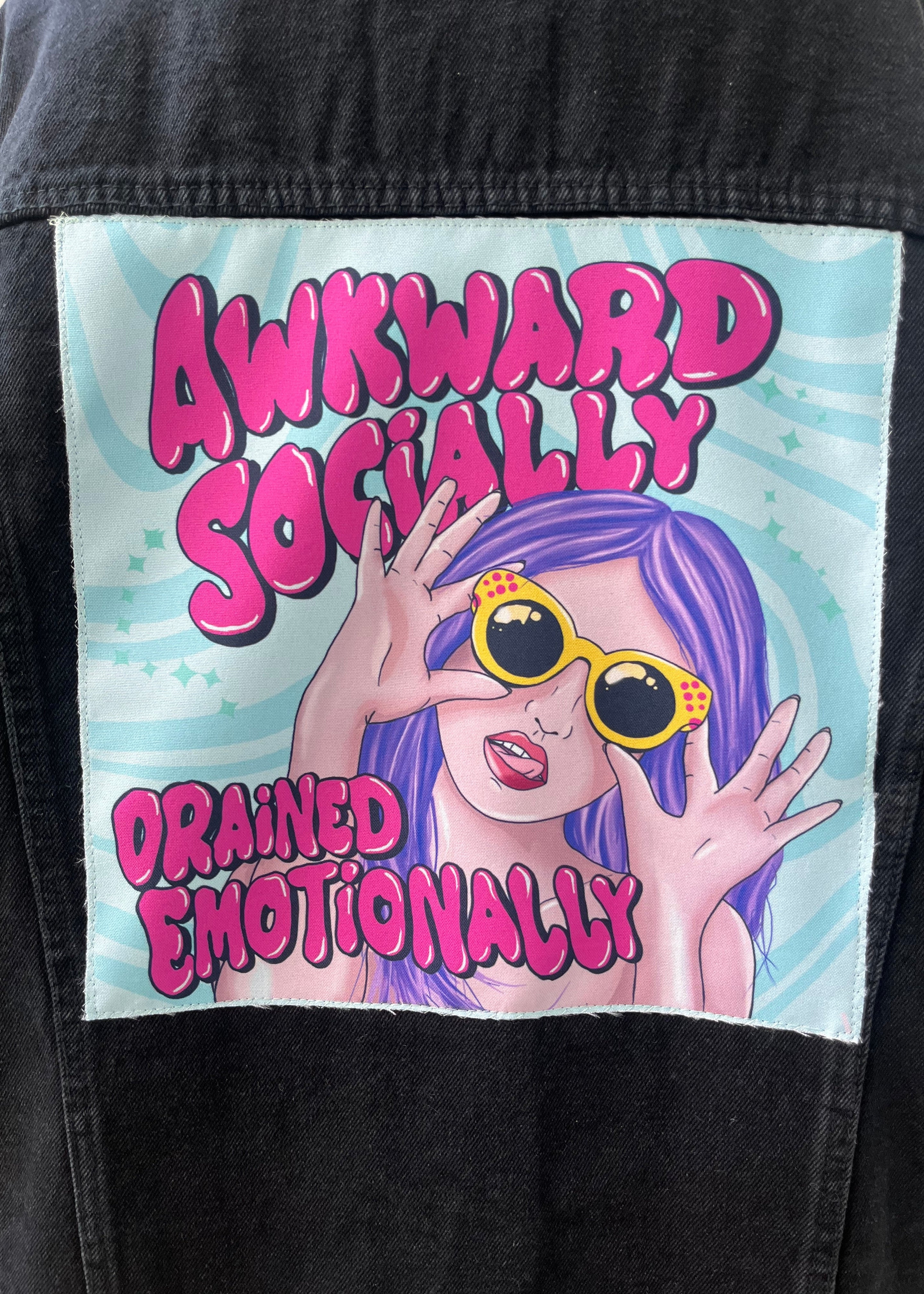 Patch with cartoon character and text 'Awkward Socially Drained Emotionally' on a black background