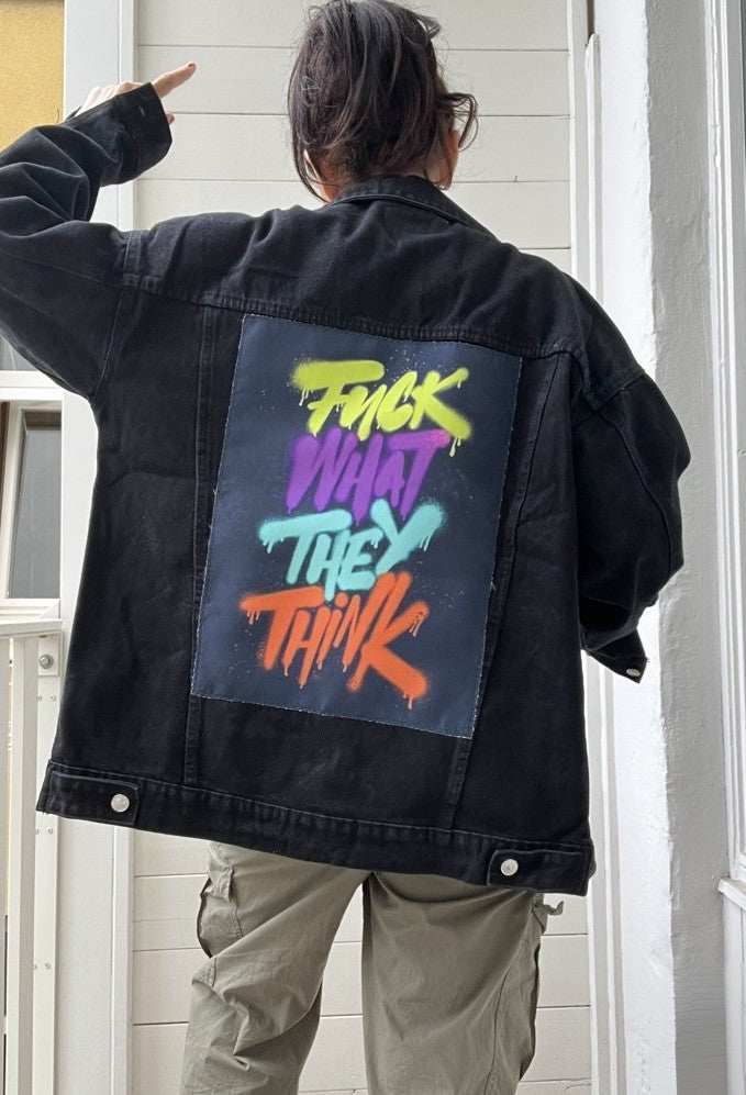 Person wearing a black jacket with colorful text on the back, standing in front of a white door.
