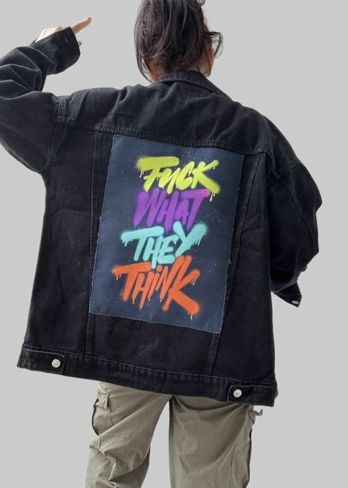 Person wearing a black jacket with colorful text on the back, standing in front of a white door.