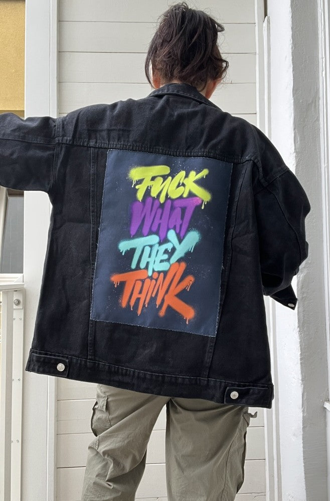 Person wearing a black jacket with colorful text on the back, standing in a neutral setting.