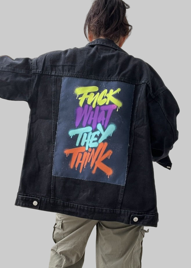 Person wearing a black jacket with colorful text on the back, standing in a neutral setting.