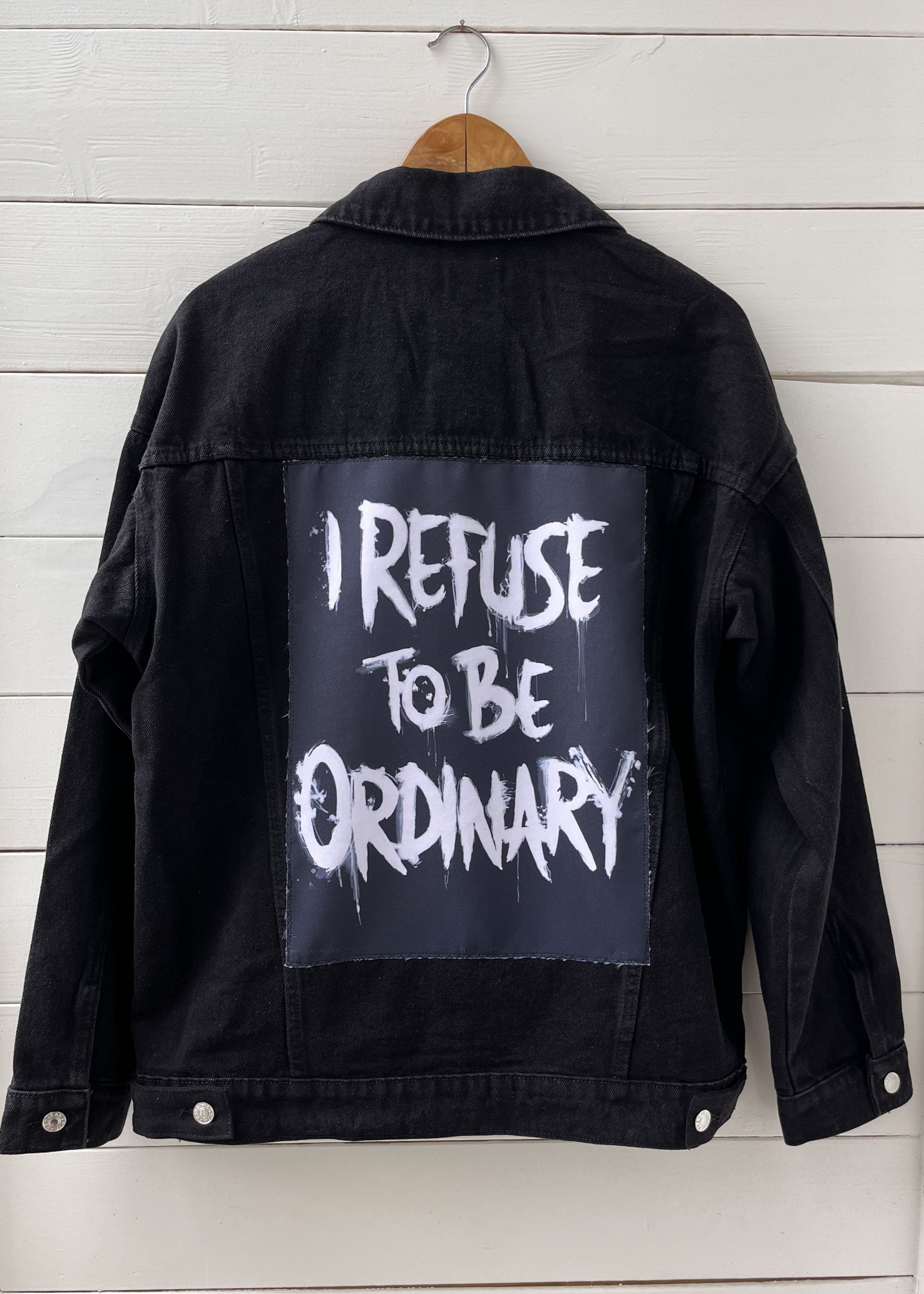 Black jacket with 'I Refuse to be Ordinary' text on a wooden background