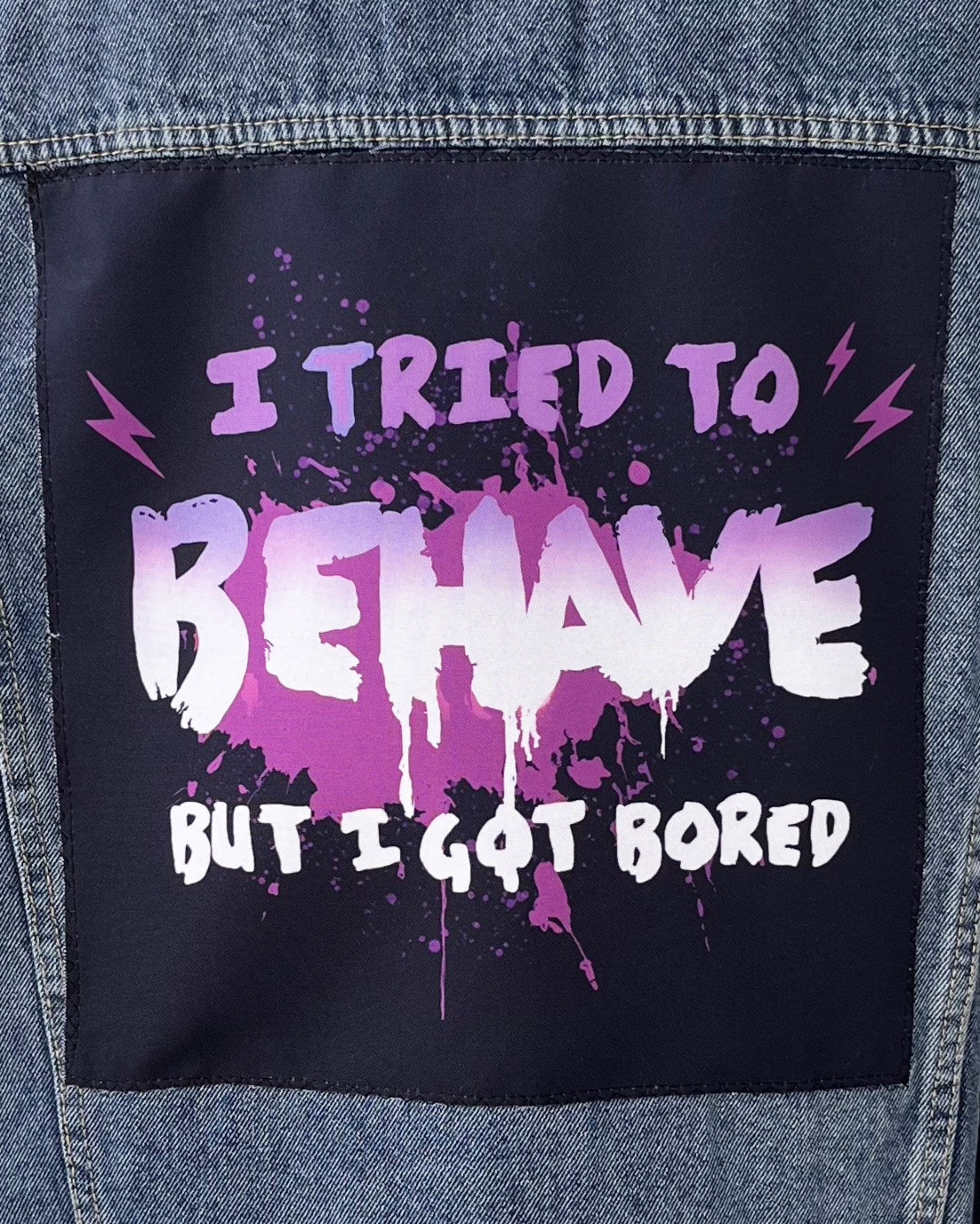 Denim jacket with a patch that says 'I tried to behave but I got bored' in purple and white text.