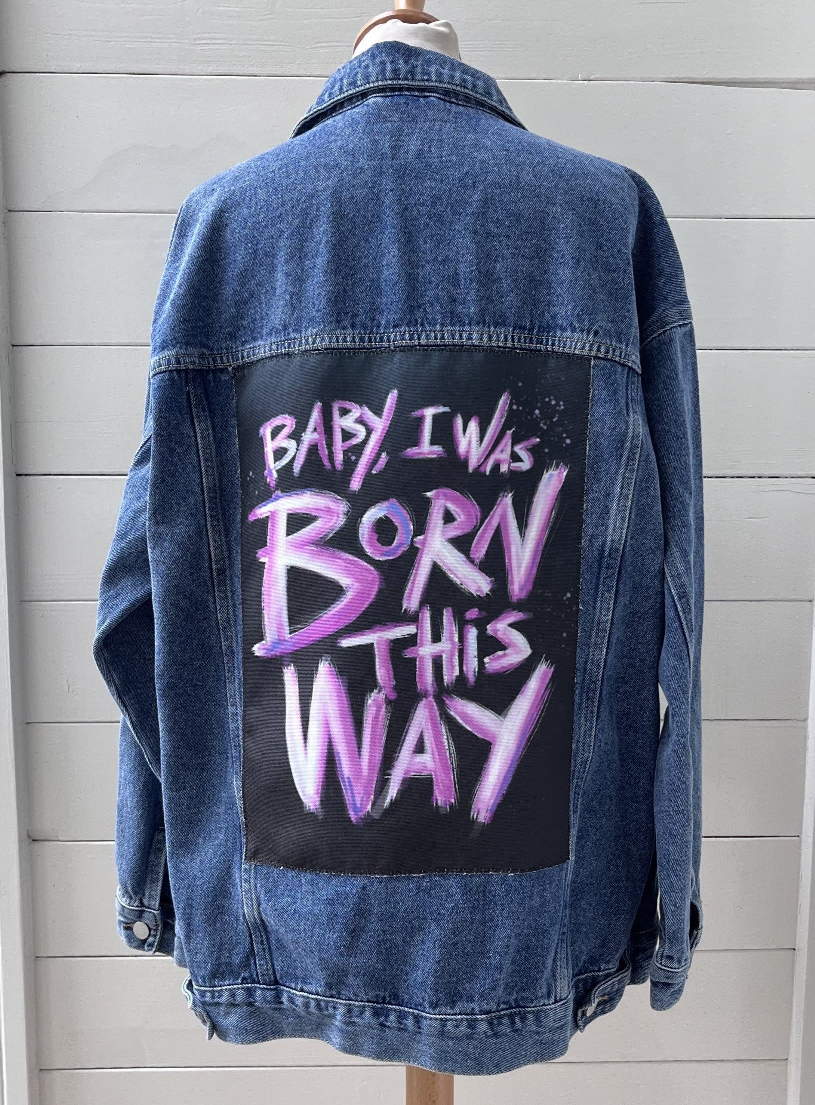 Denim jacket with 'Baby I was born this way' text on a mannequin against a light gray background