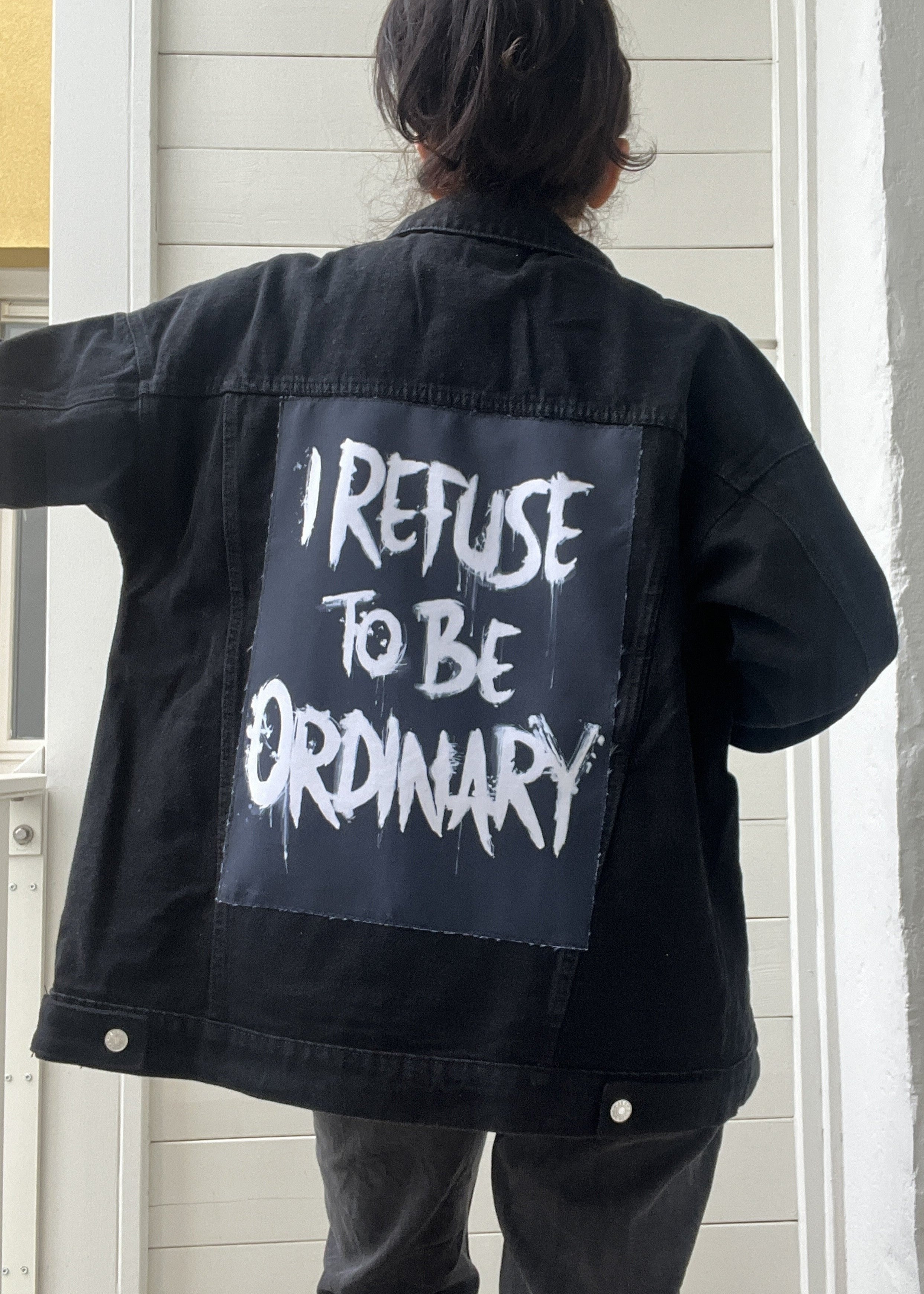 Person wearing a black jacket with 'I Refuse to be Ordinary' text on the back.