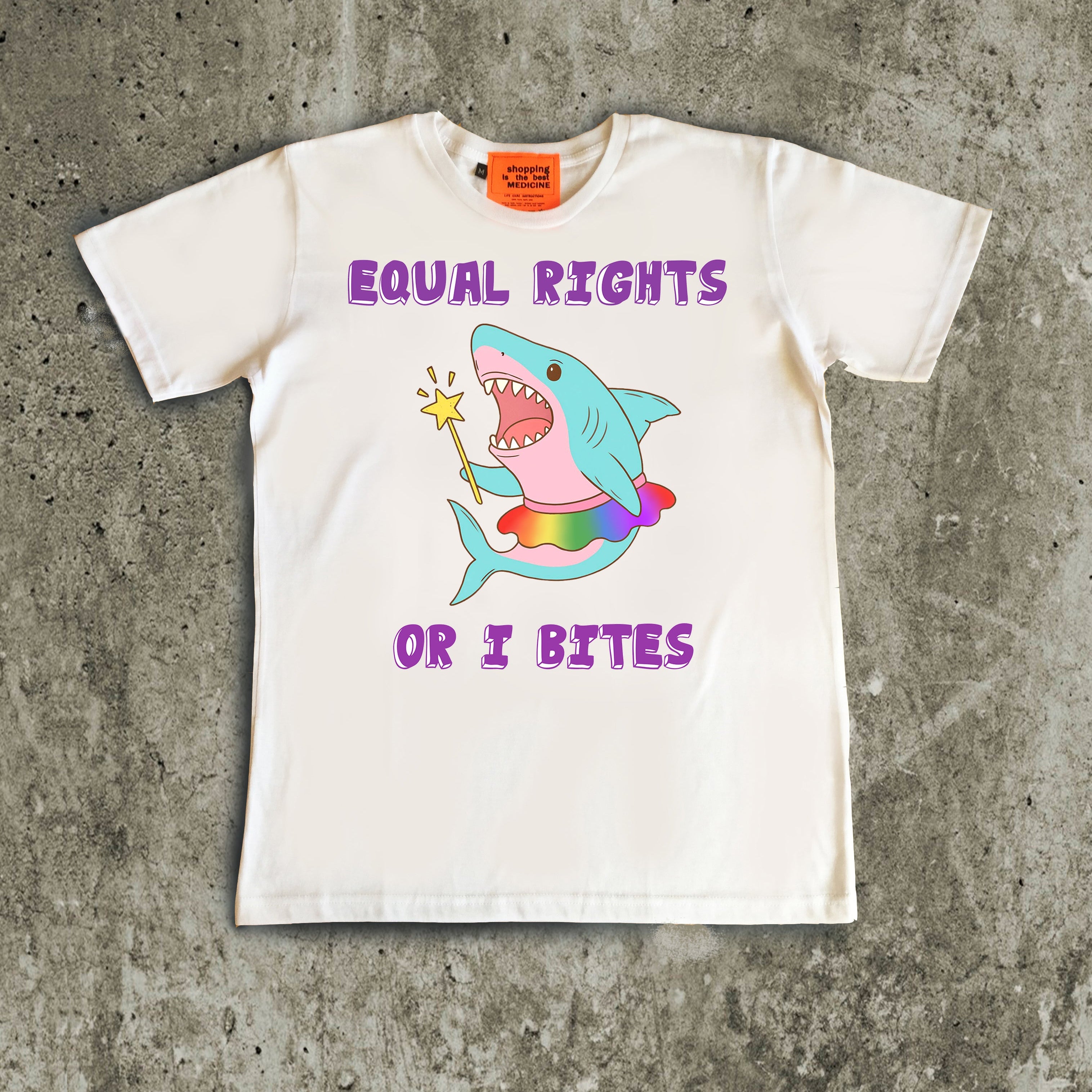 White t-shirt with a colorful shark graphic and text on a concrete surface, gay pride illustration