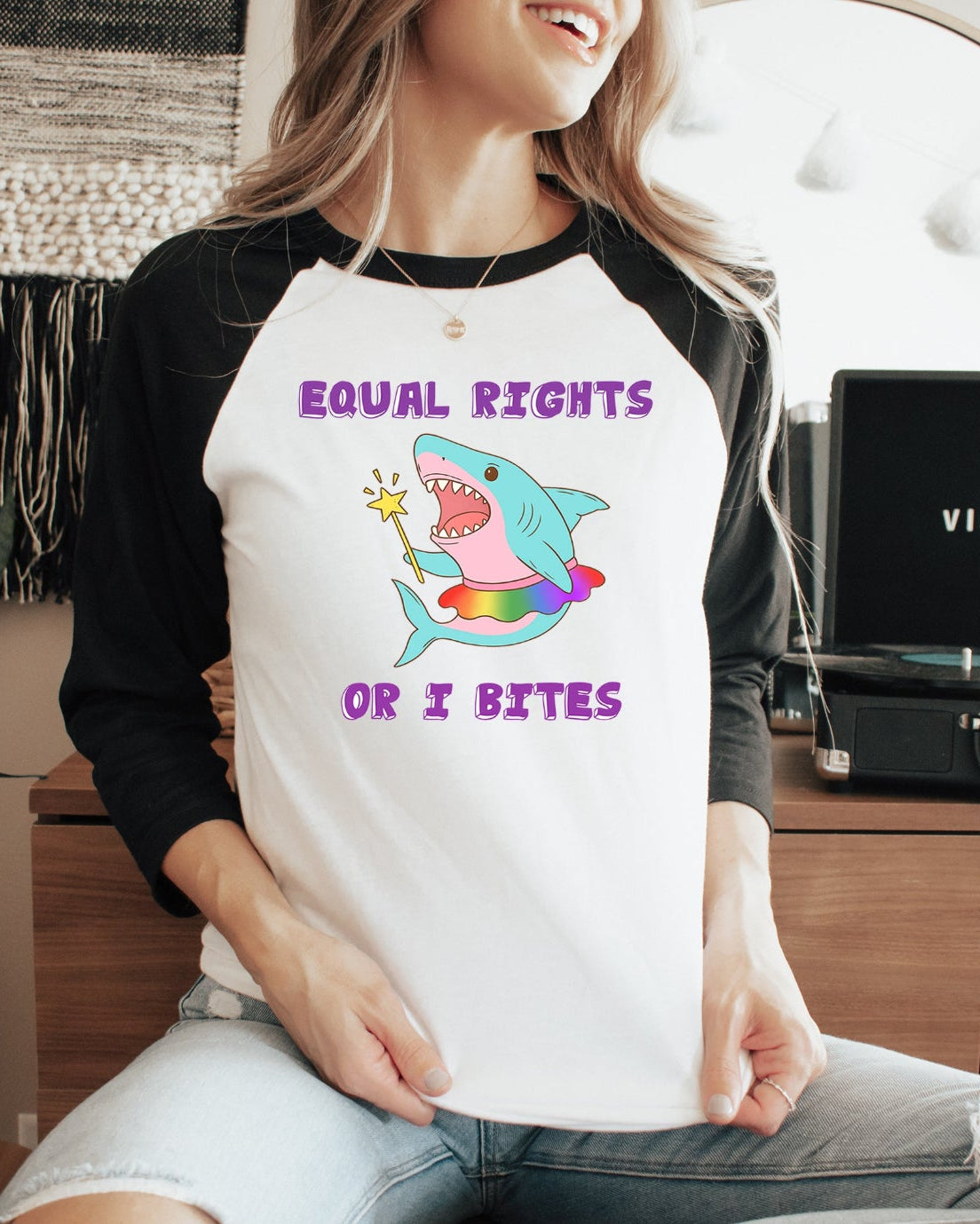 Person wearing a shirt with a shark graphic and text, sitting in a room with a plant and record player.