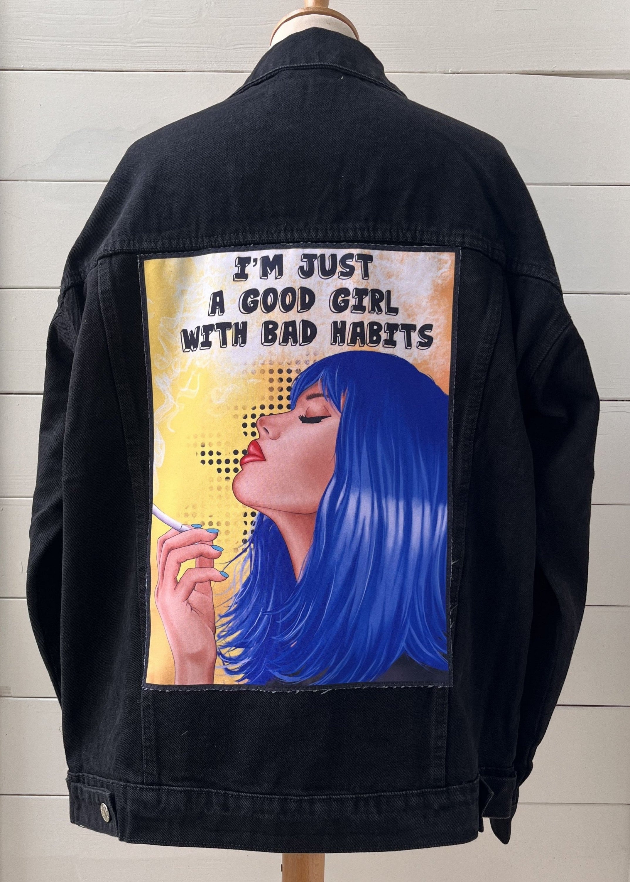 Black jacket with a graphic design of a woman smoking and text on the back, displayed against a light wooden panel background.