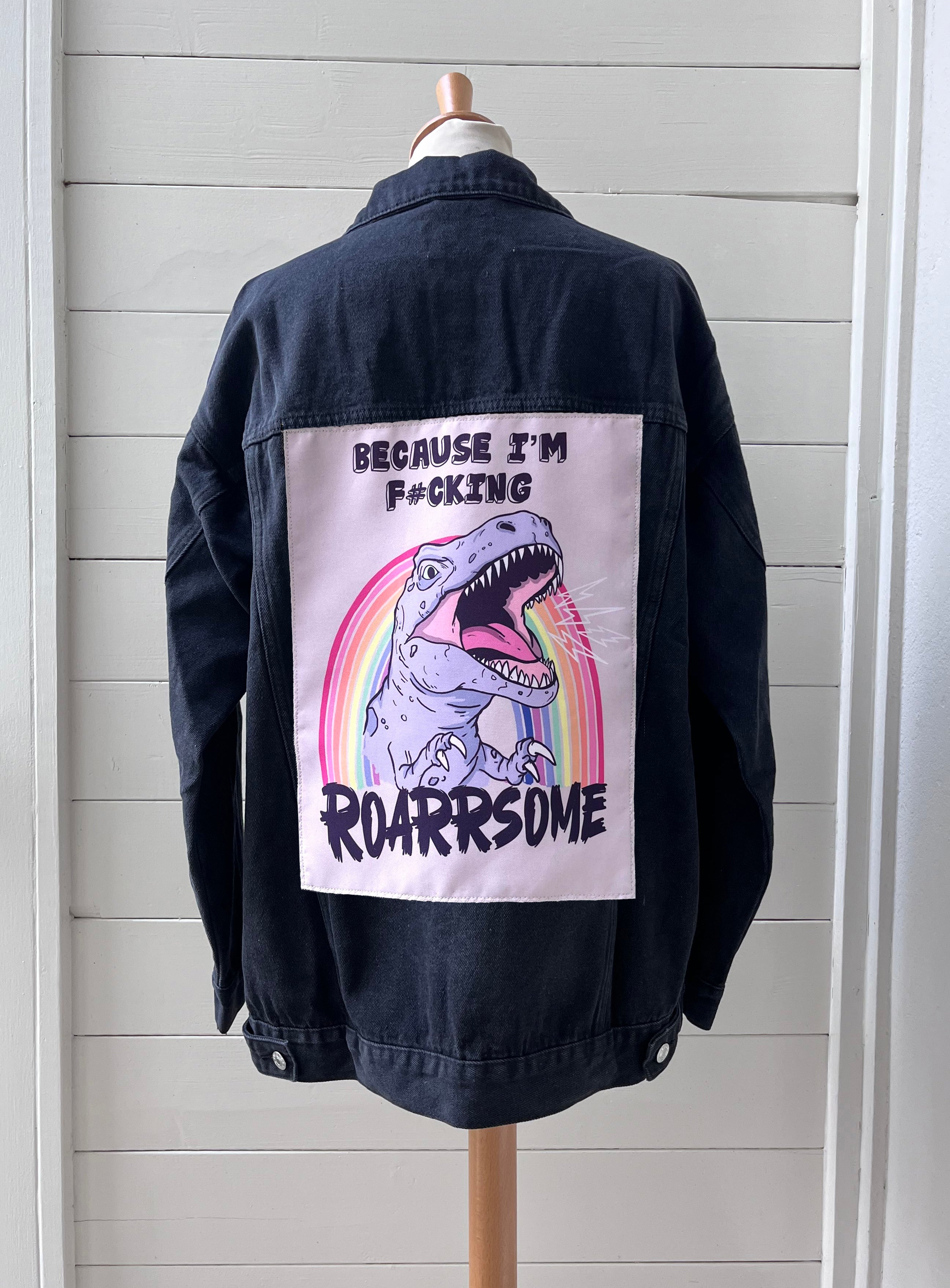 Black jacket with a graphic design on the back featuring a dinosaur and text, displayed on a mannequin against a white wall.