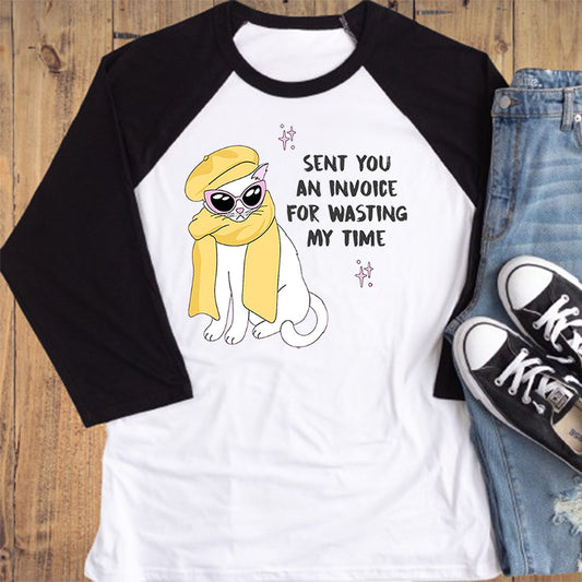 White baseball shirt with black sleeves, cartoon character, and text, paired with jeans and sneakers on a wooden surface.