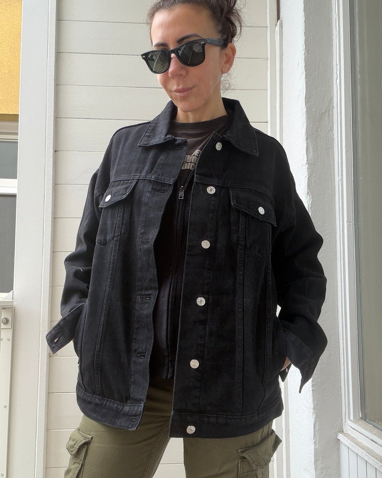 Person wearing a black denim jacket and green cargo pants standing indoors.