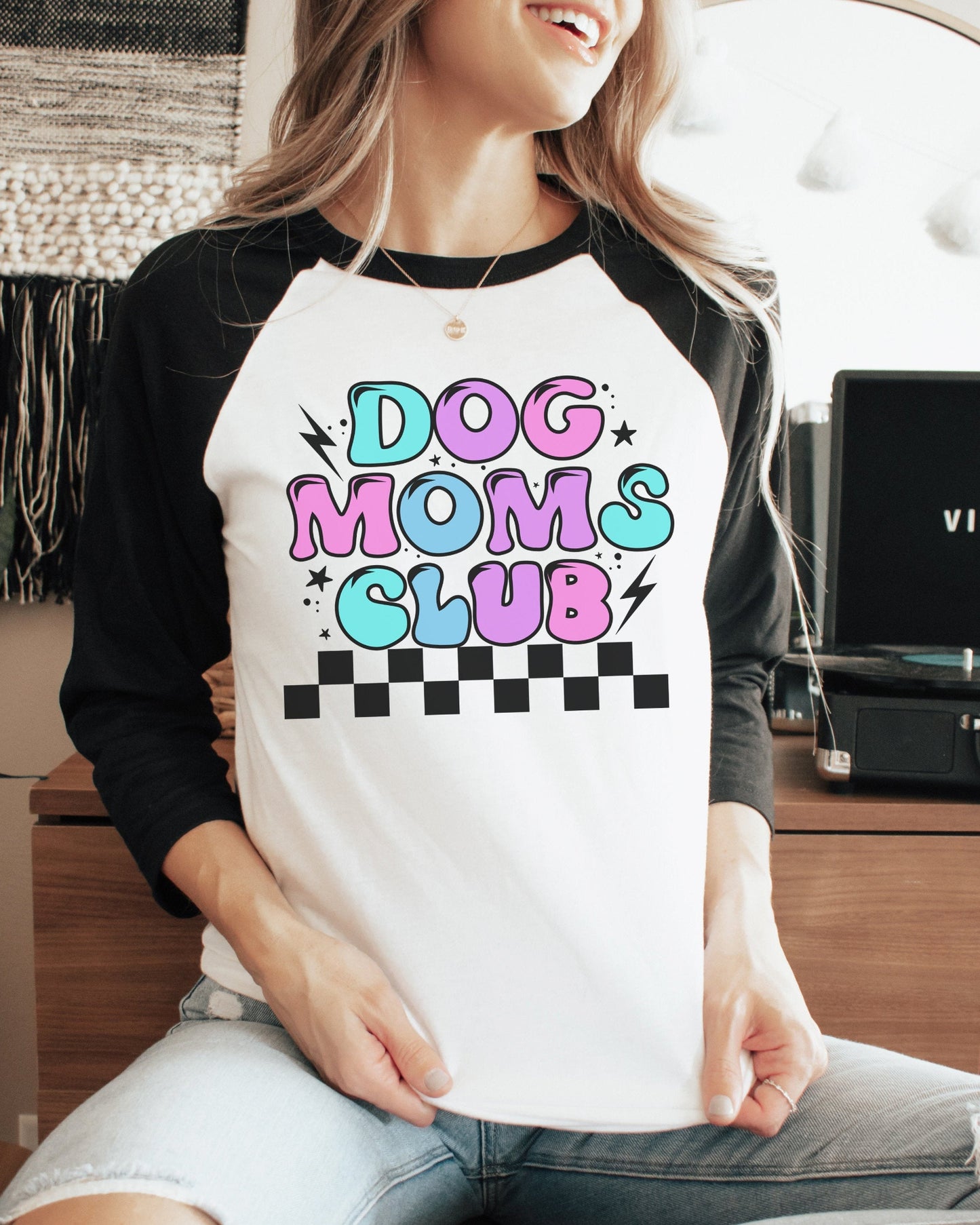 A person wearing a white 3/4 sleeves t-shirt with a colorful 'DOG MOMS CLUB' graphic print.