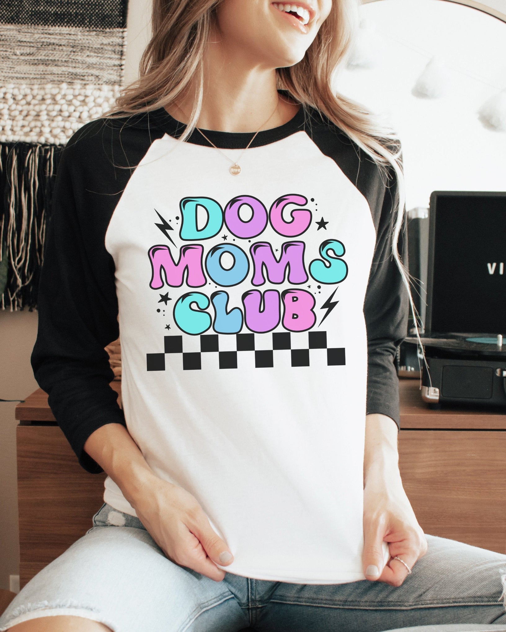 A person wearing a white 3/4 sleeves t-shirt with a colorful 'DOG MOMS CLUB' graphic print.