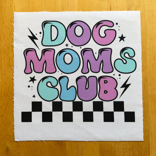 Fabric patch with 'Dog Moms Club' text on a wooden surface