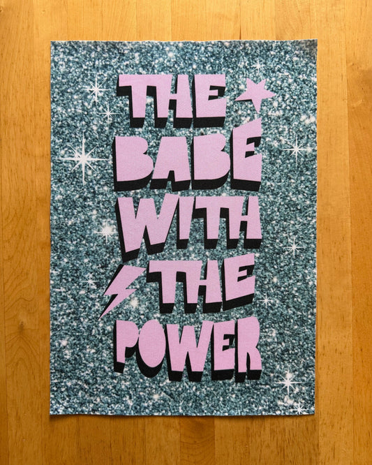 Glittery poster with 'The Babe with the Power' text on a wooden surface
