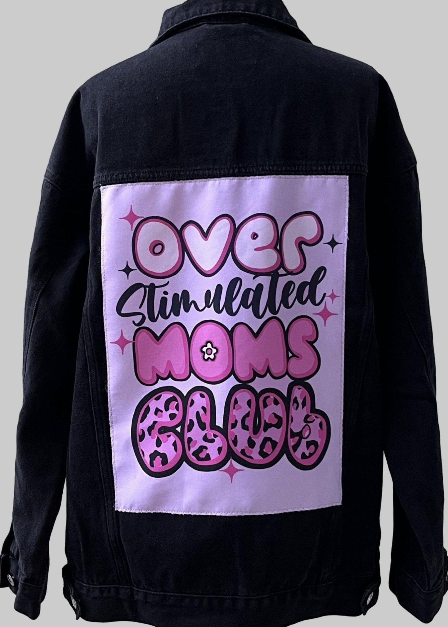 Black denim jacket with a pink graphic on the back against a white wooden panel background