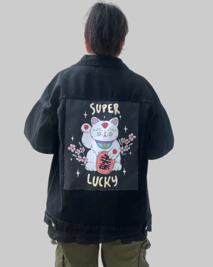 Person wearing a black jacket with a lucky cat design on the back against a plain background