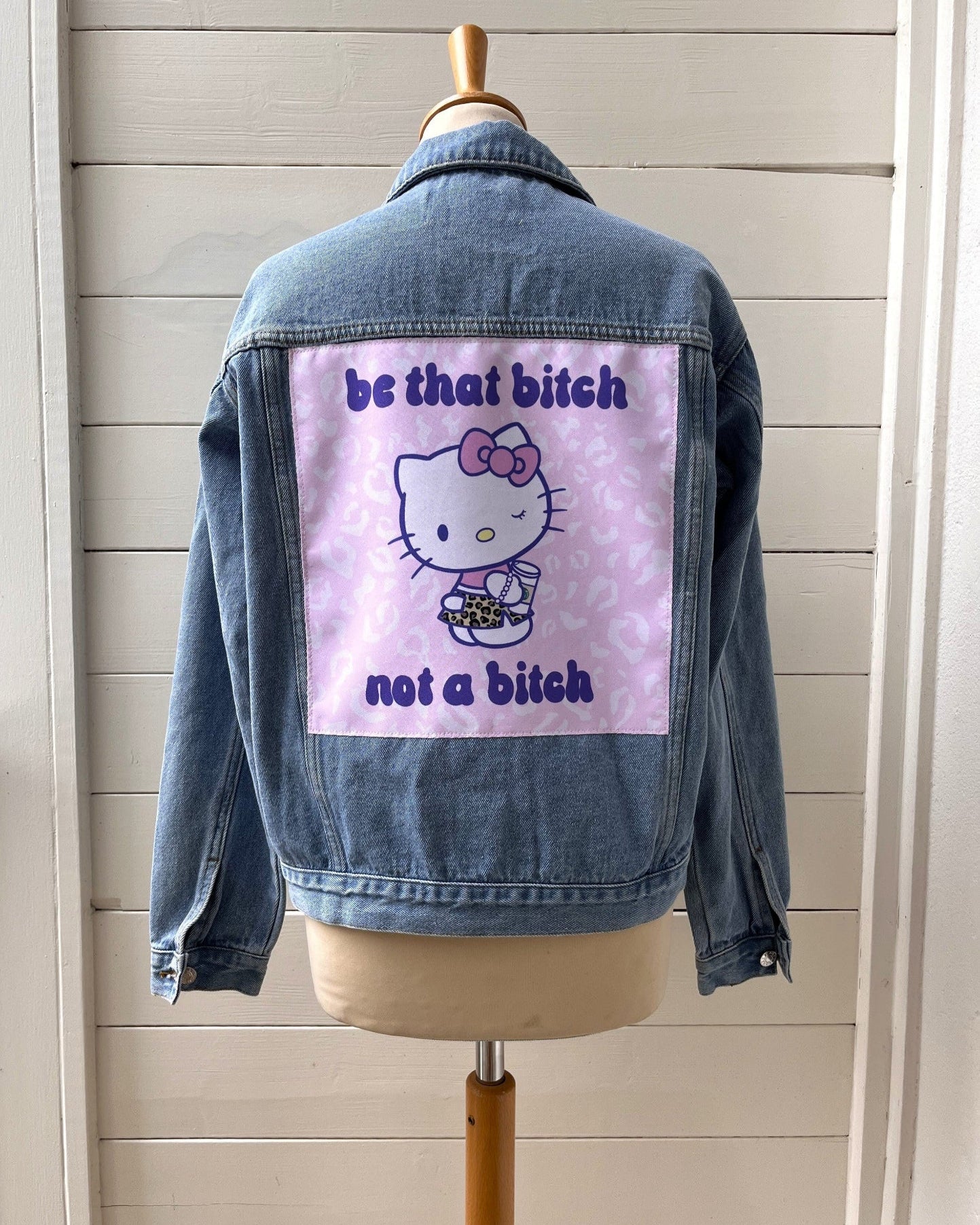 Denim jacket with a graphic design on a mannequin against a wooden panel background