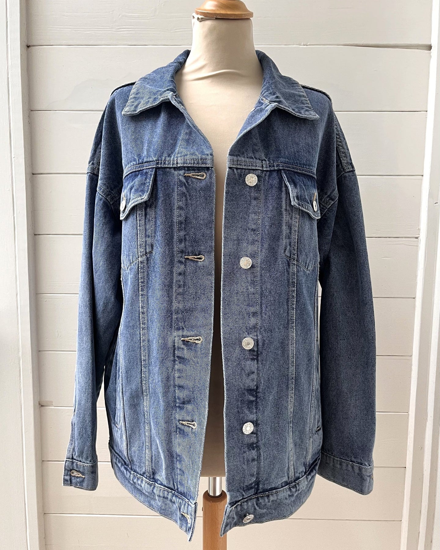 Blue denim jacket on a mannequin against a white wooden panel background