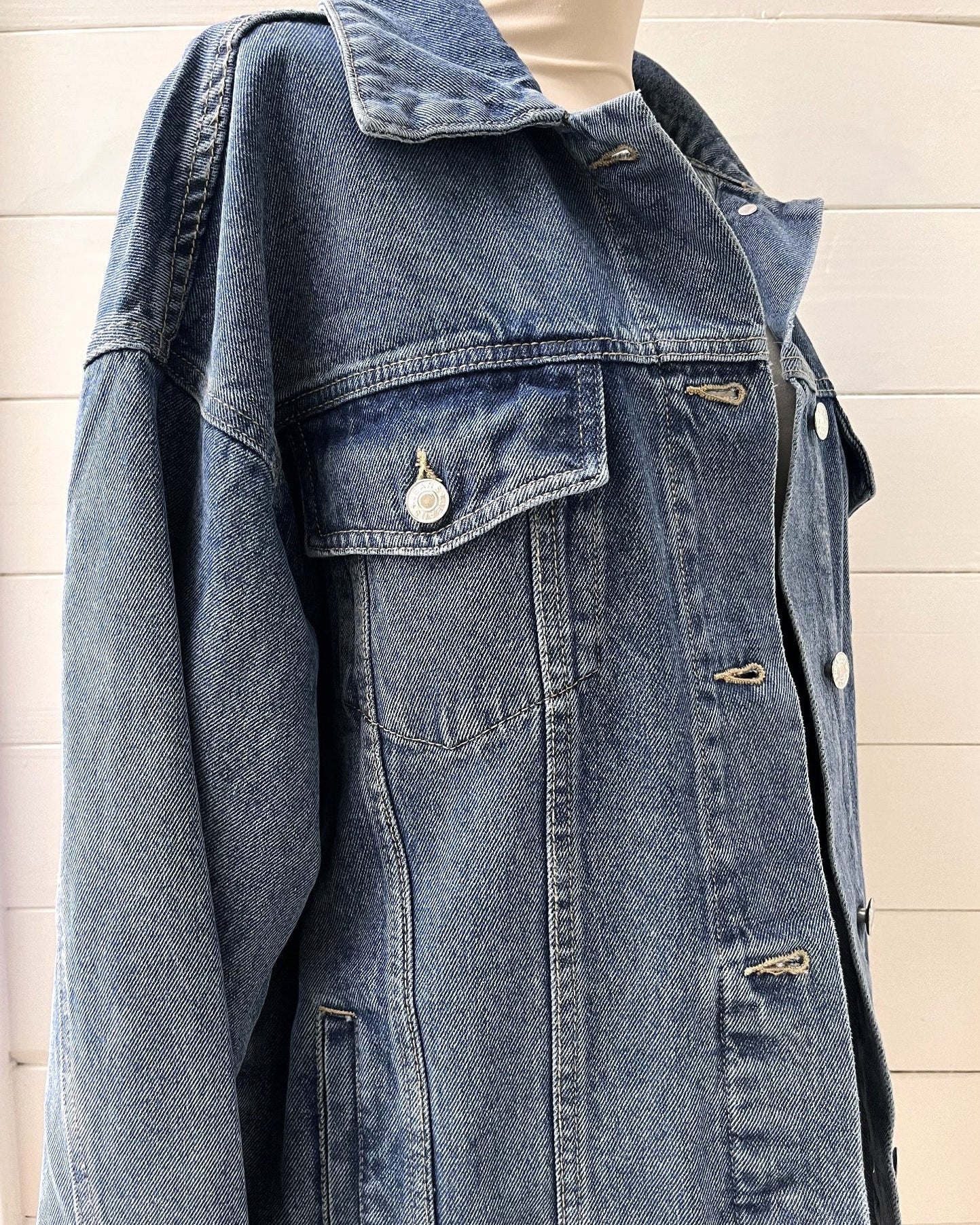 Blue denim jacket on a mannequin against a wooden panel background