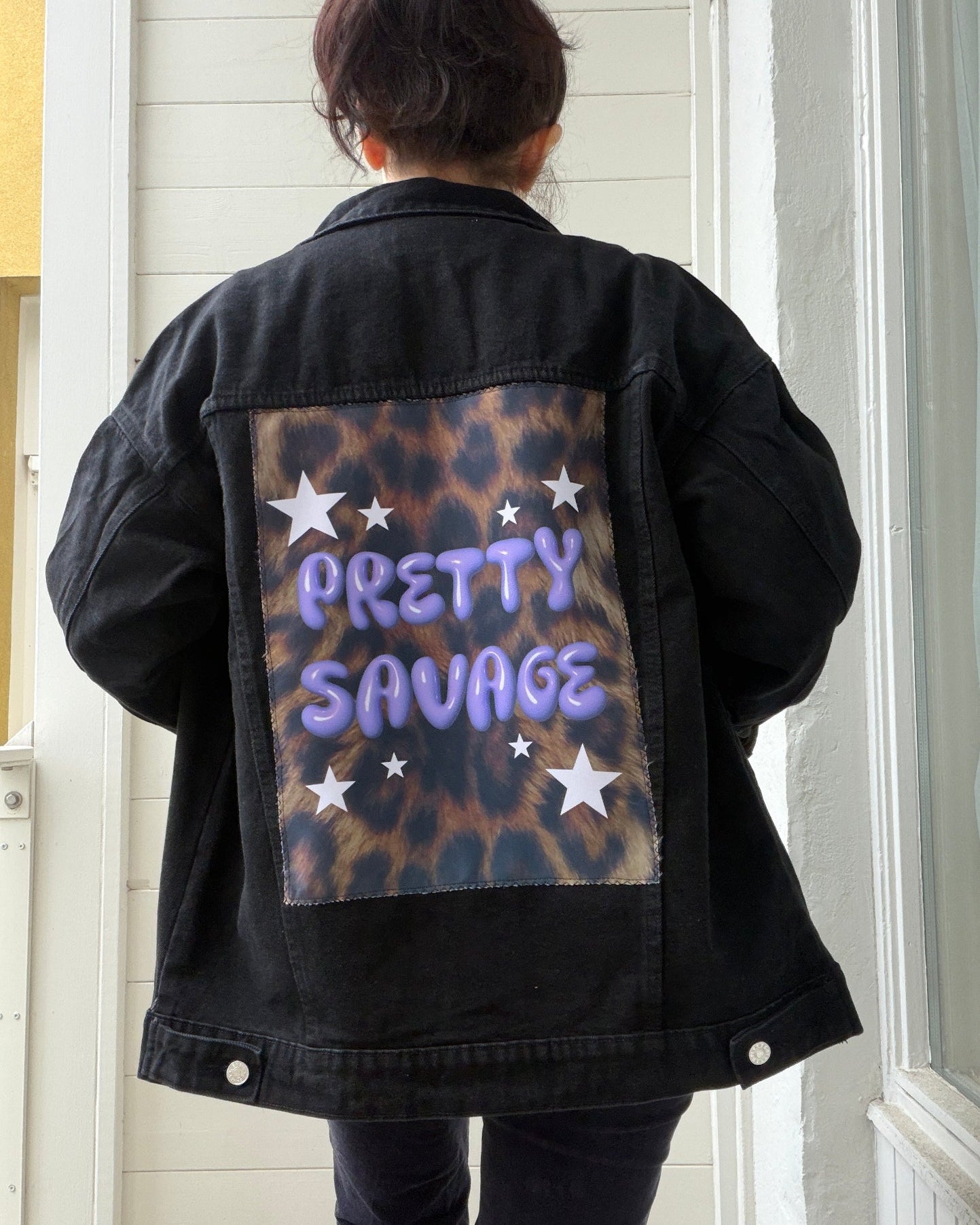Black denim jacket with leopard print patch and text worn by a person indoors.