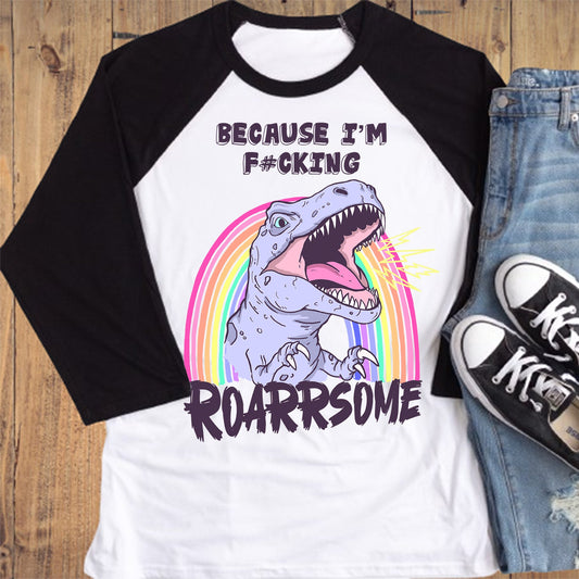 Raglan shirt with dinosaur graphic and text, jeans, and sneakers on a wooden surface