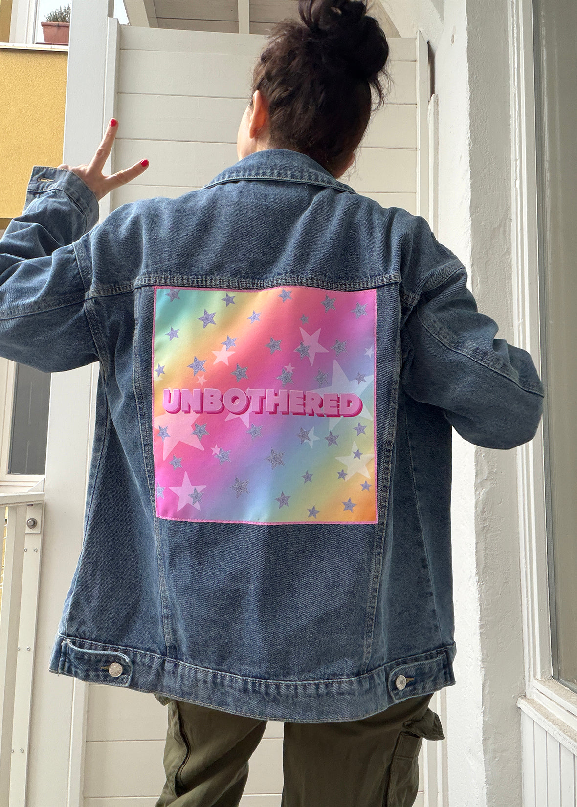 Person wearing a denim jacket with a colorful back design and 'UNBOtherED' text.