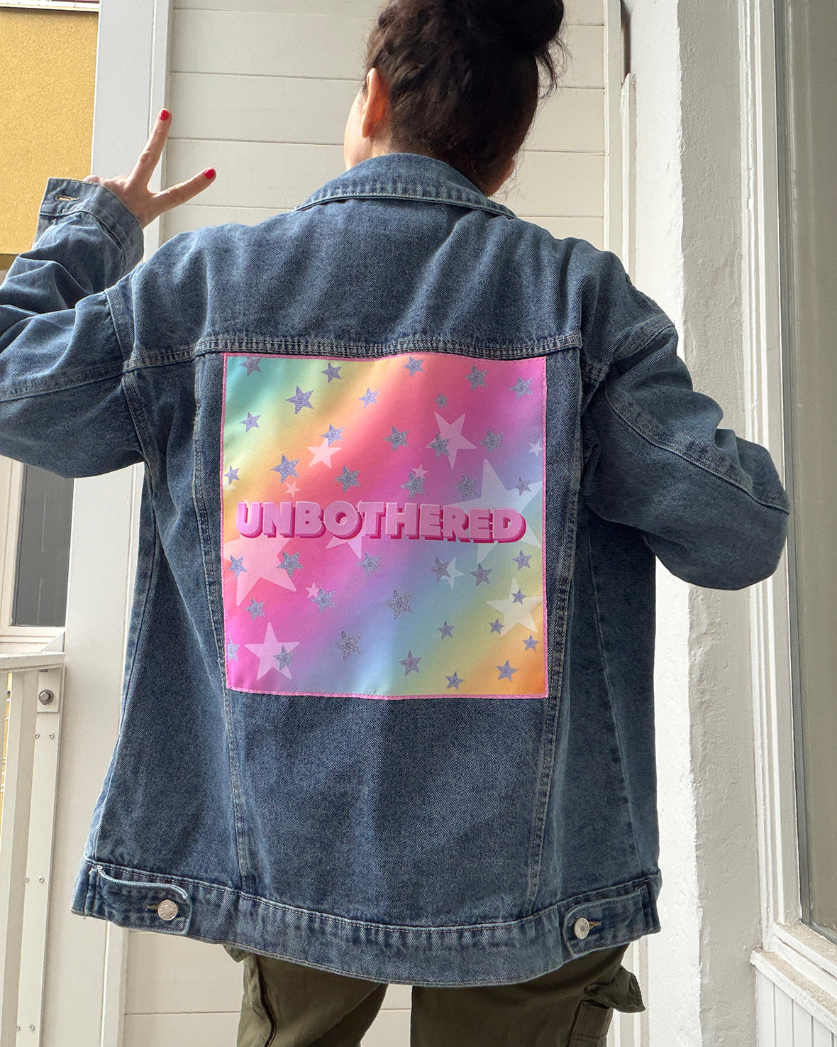 Person wearing a denim jacket with a colorful back design and 'UNBOtherED' text.