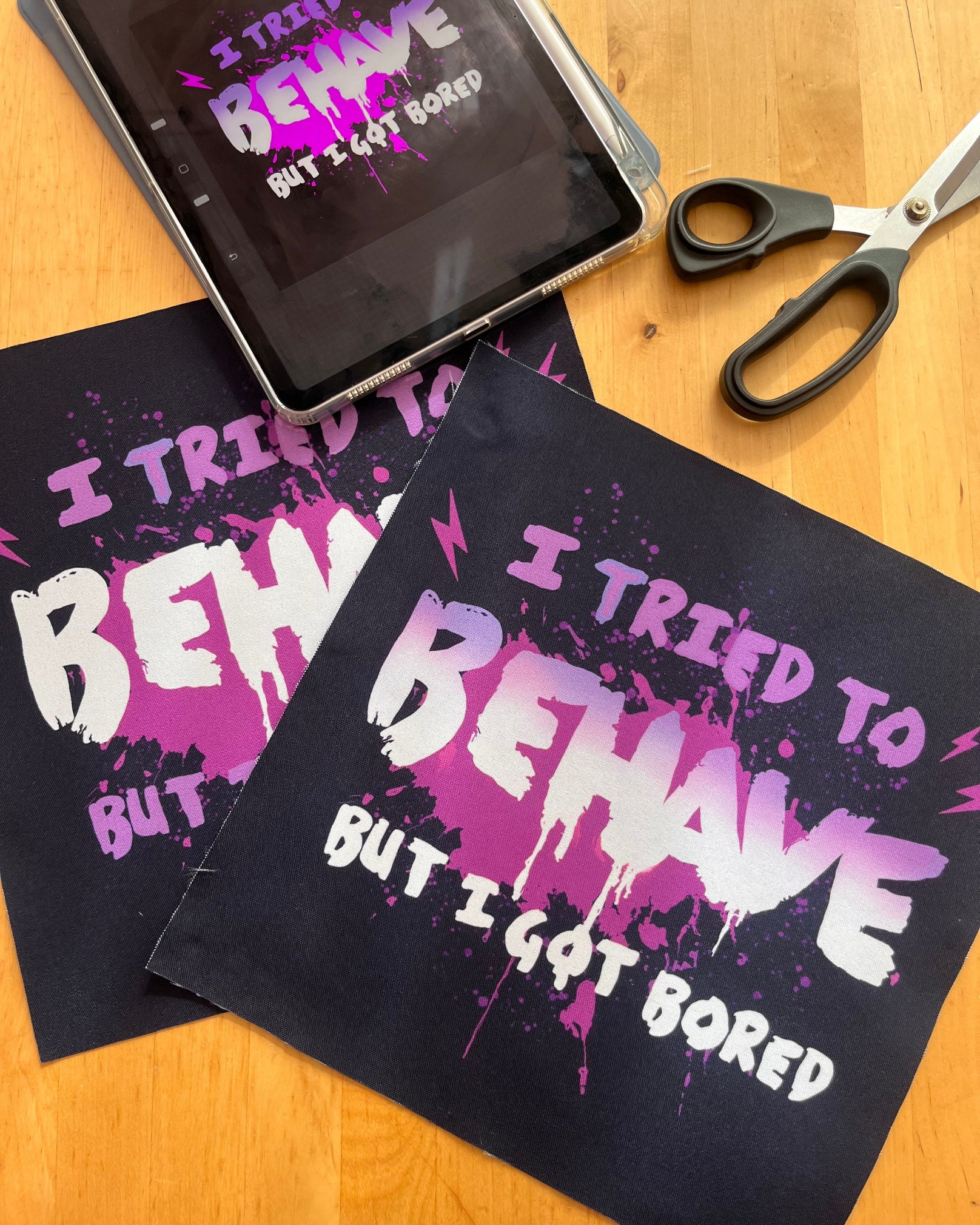 Black towel with purple and white text on a wooden surface with scissors and a phone.