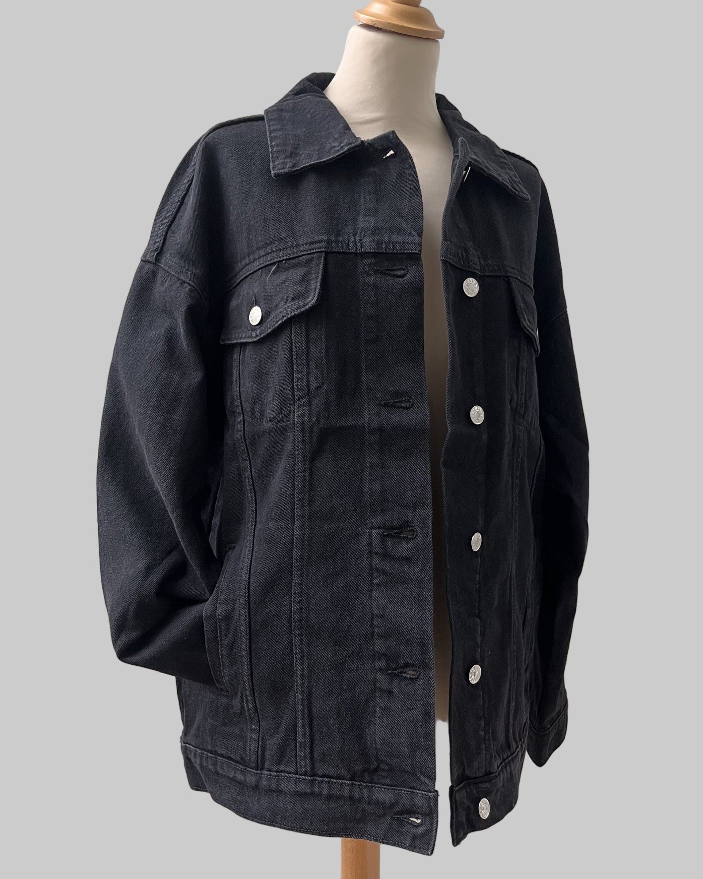 Black denim jacket on a mannequin against a white wooden panel background