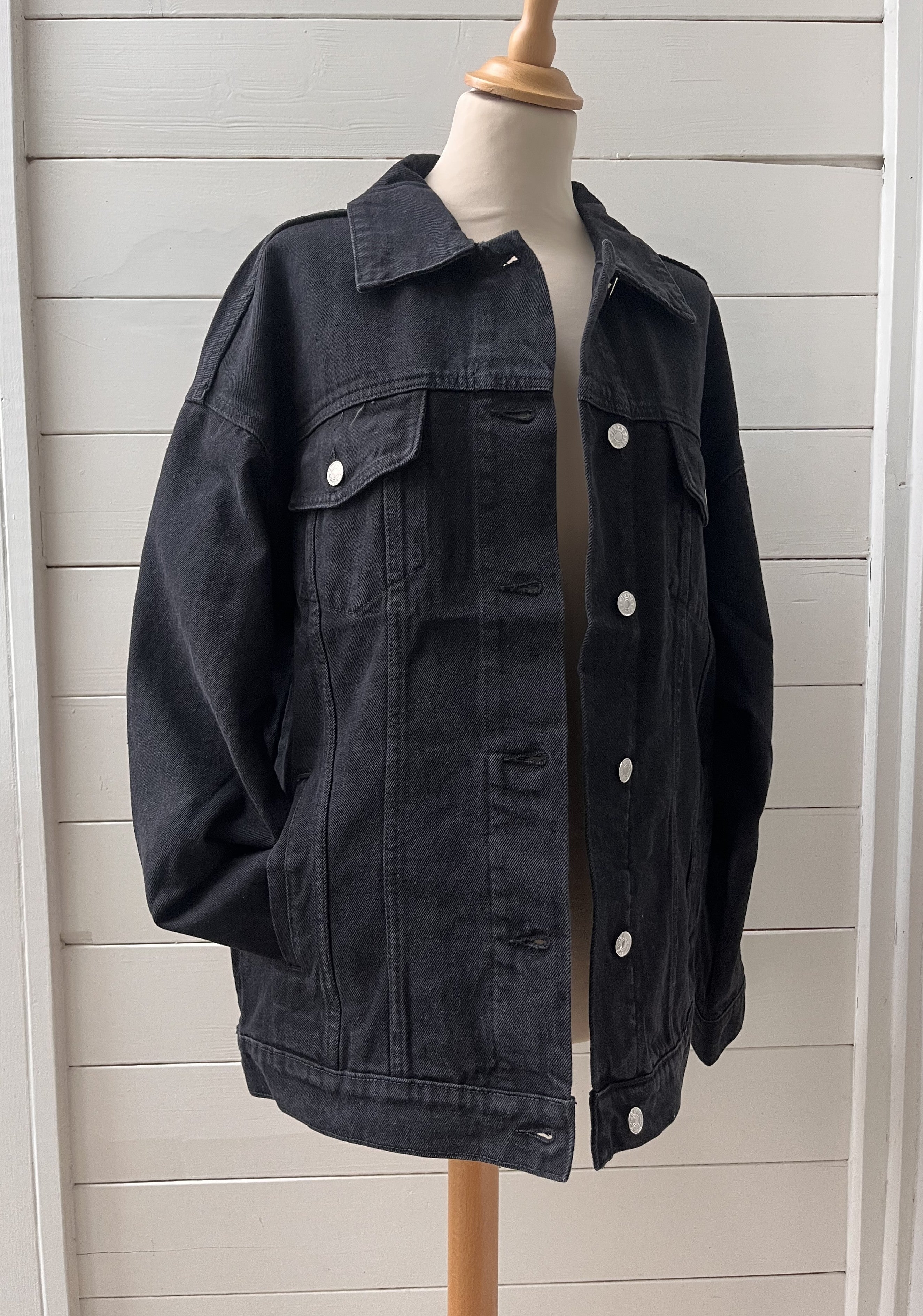 Black denim jacket on a mannequin against a white wooden panel background