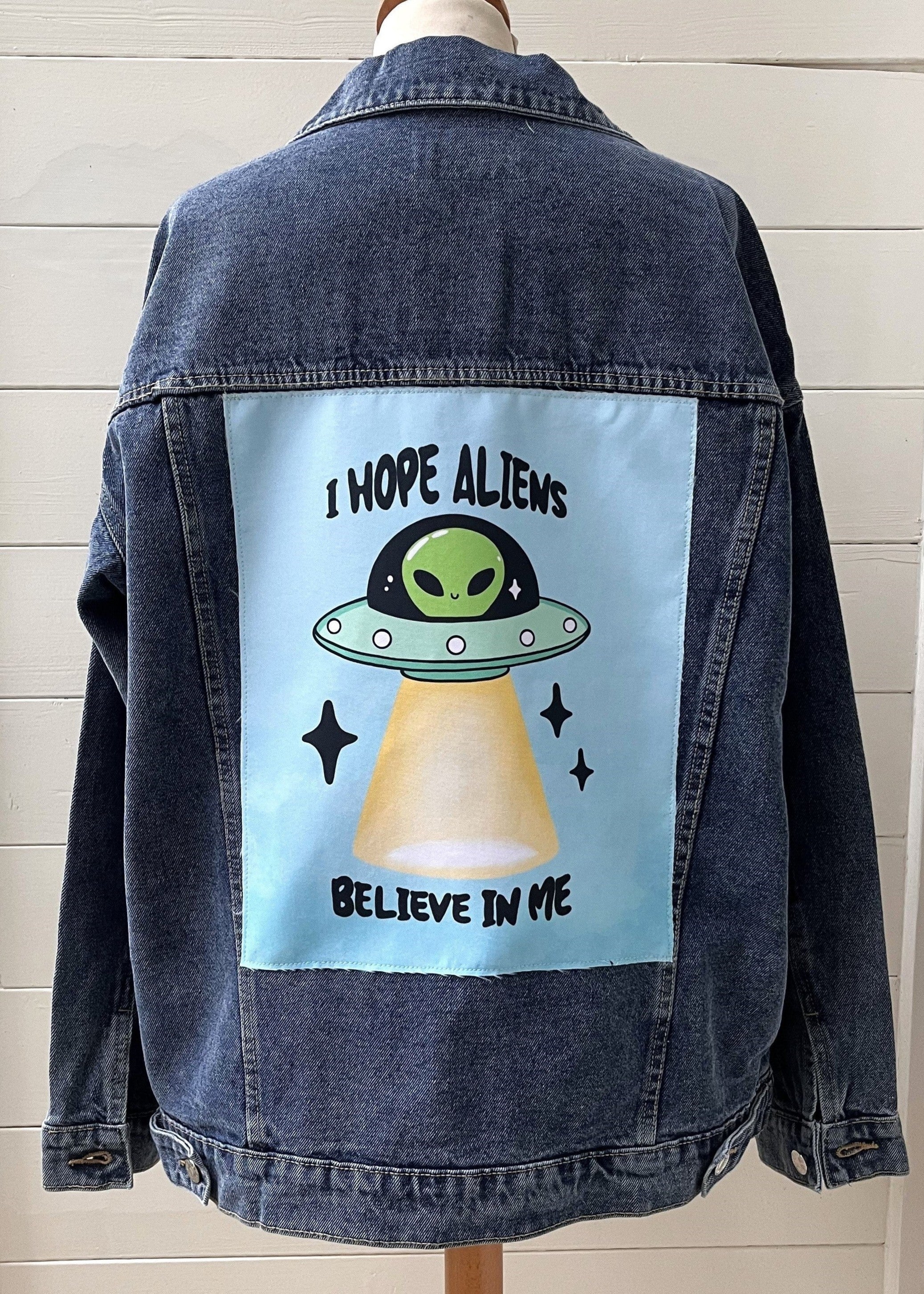 Denim jacket with alien graphic and text on a mannequin against a white wall.