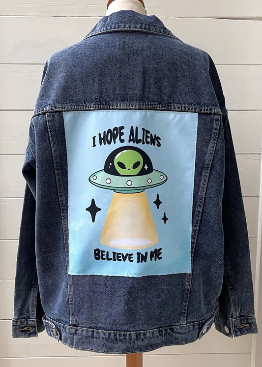 Denim jacket with alien graphic and text on a mannequin against a white wall.