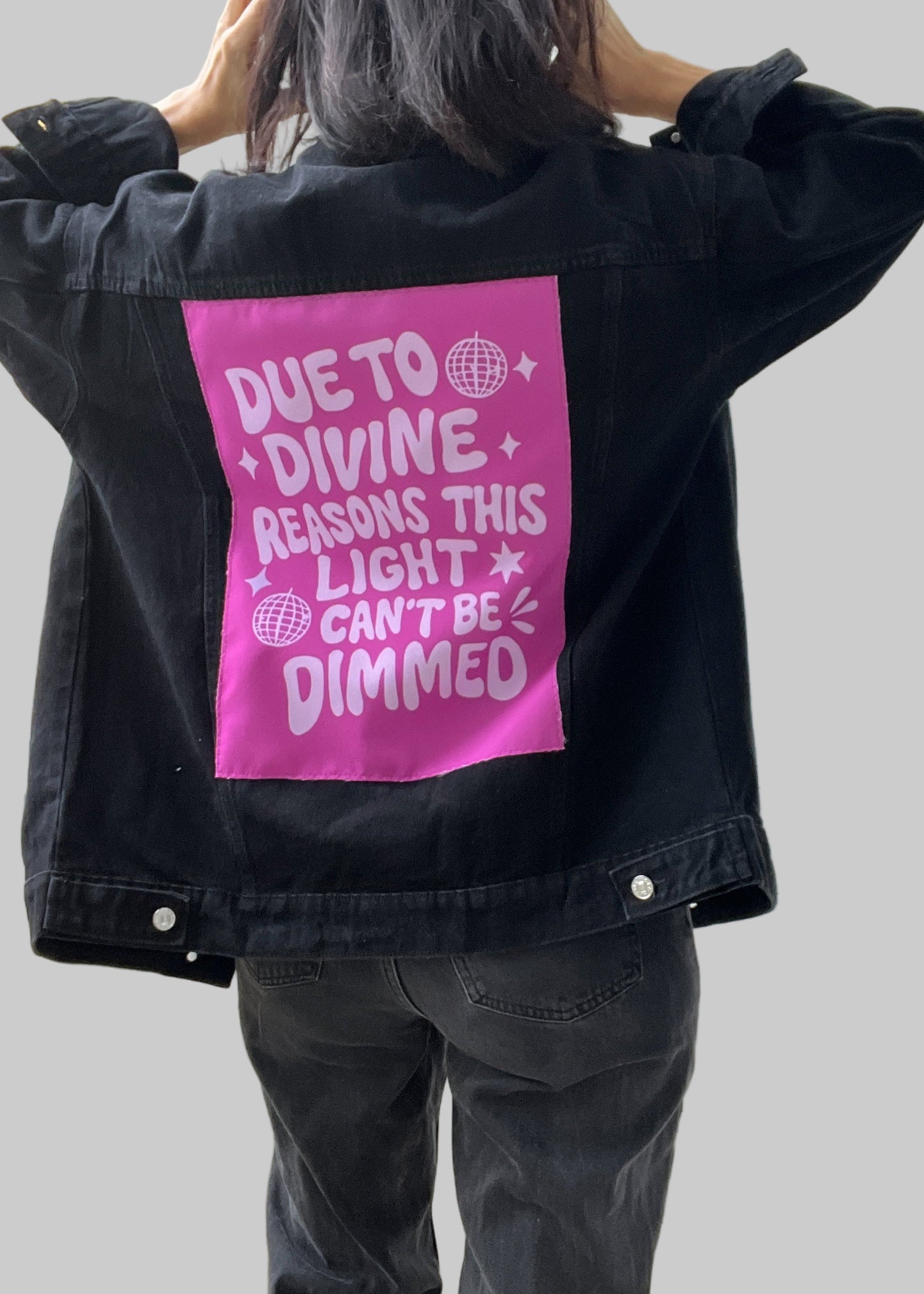 Person wearing a black jacket with a pink graphic on the back, standing indoors.