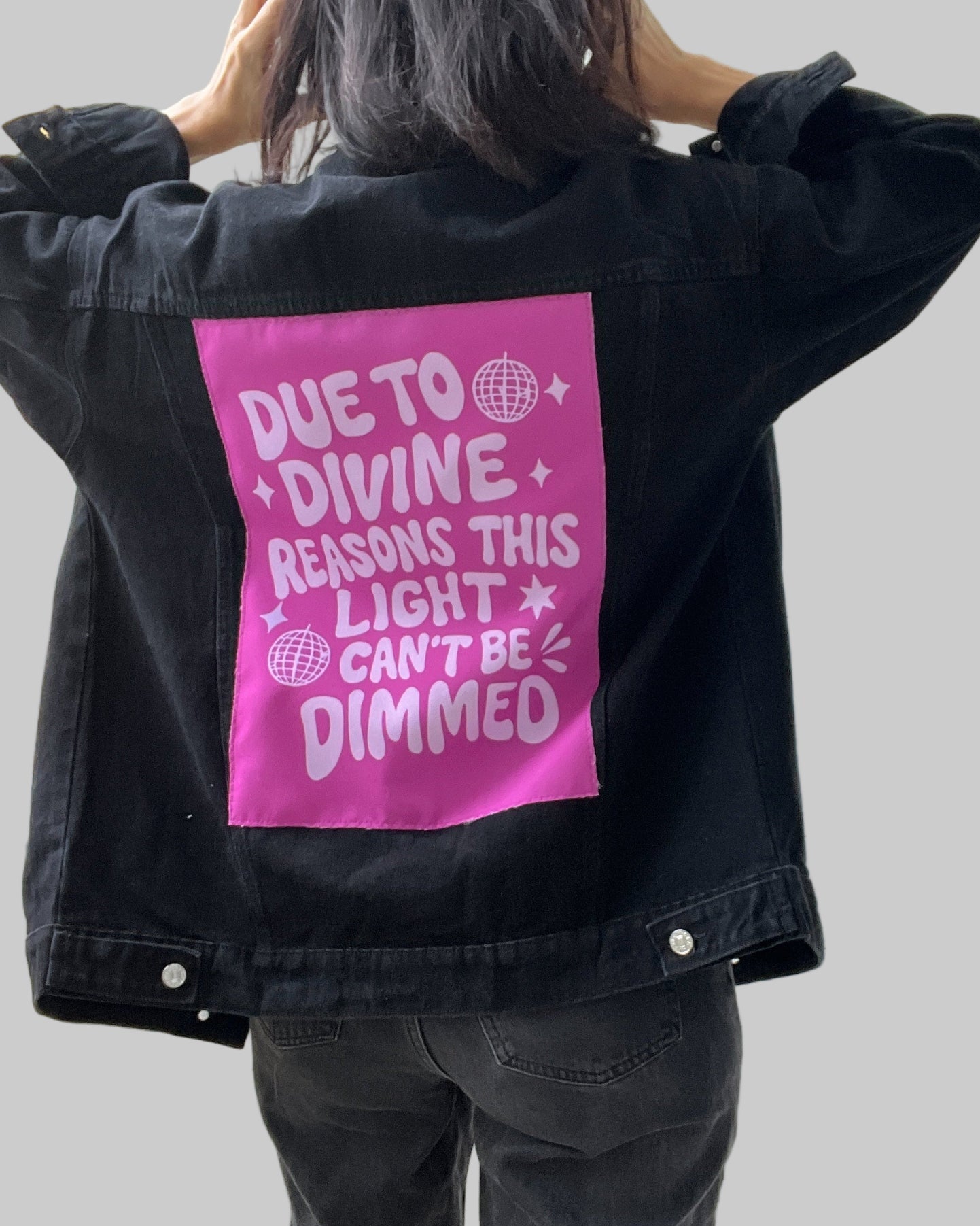 Person wearing a black jacket with a pink graphic on the back, standing indoors.