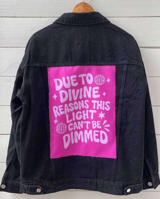 Black jacket with pink patch on a wooden hanger against a white wooden panel background