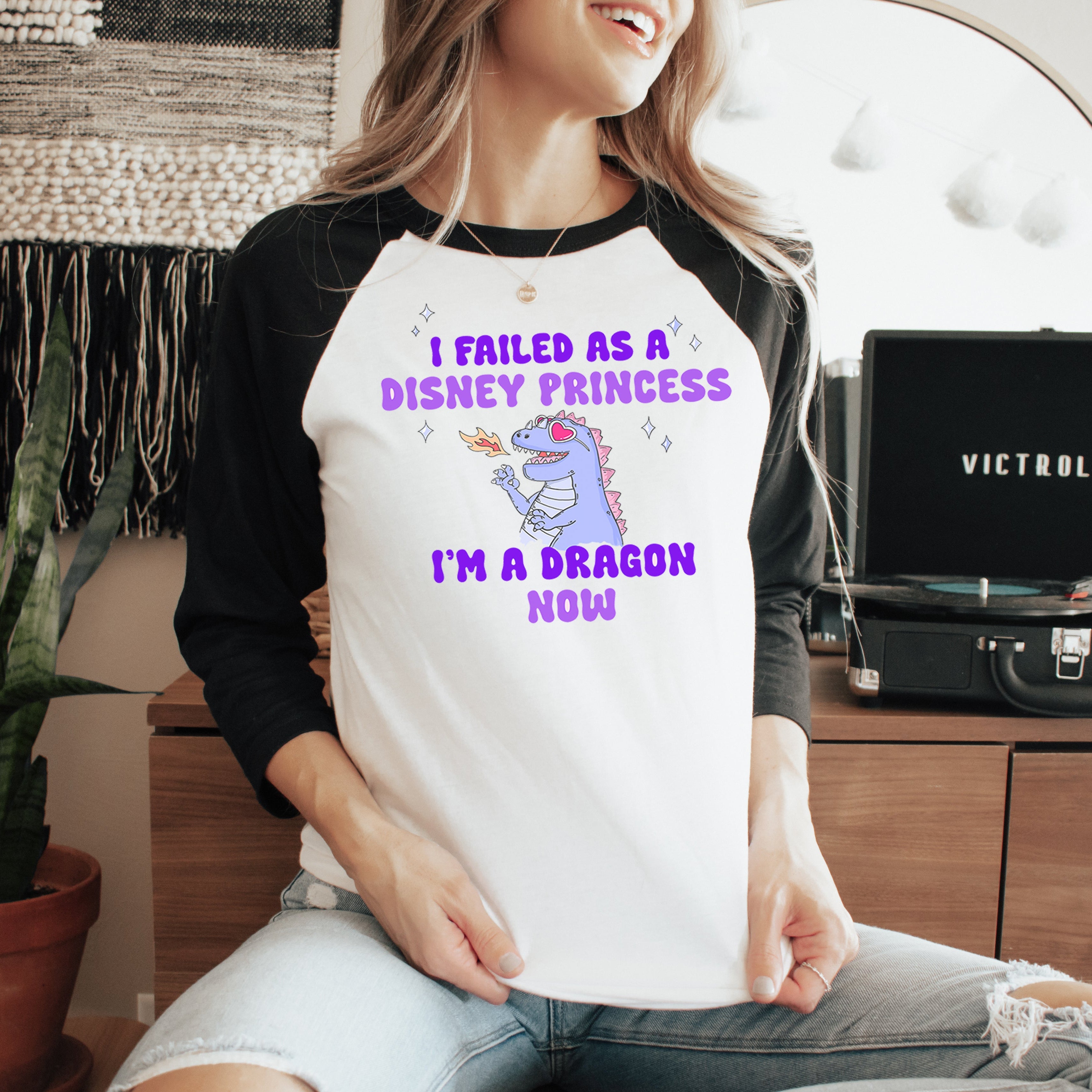 Person wearing a shirt with a humorous message about being a dragon, sitting in a room with a laptop and decor.