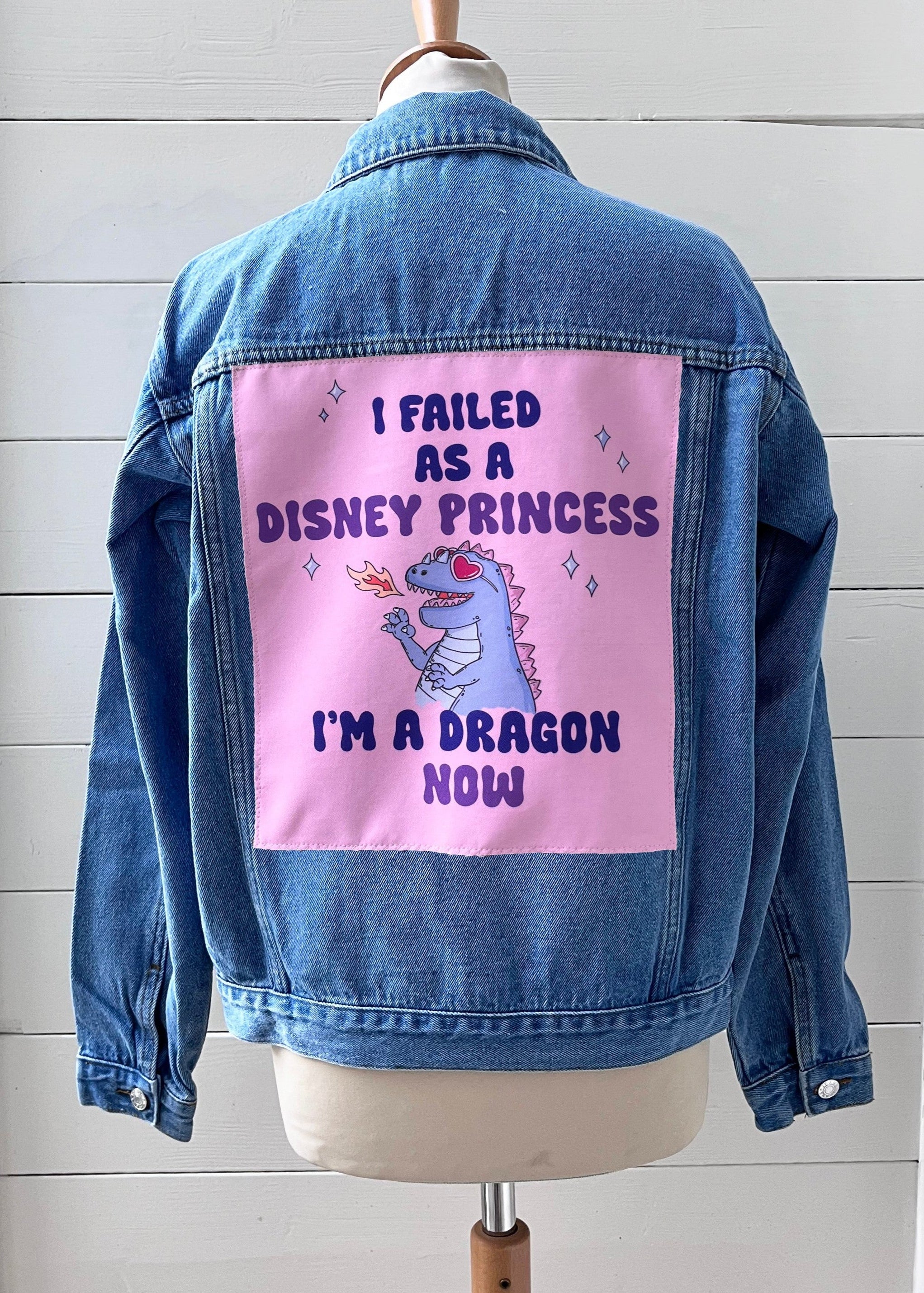 Blue denim jacket with a pink patch featuring text and a dragon illustration on a white background