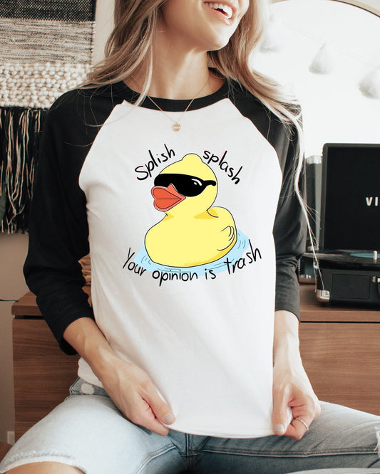 Person wearing a baseball shirt with a rubber duck graphic and text, sitting in a room with a plant and record player.